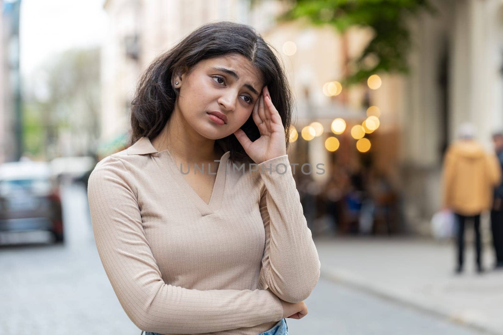 Sad unhappy Indian young woman thinks over life concerns suffers from unfair situation outdoors. Problem feeling bad annoyed burnout grief. Hispanic girl alone on urban city street. Town lifestyles