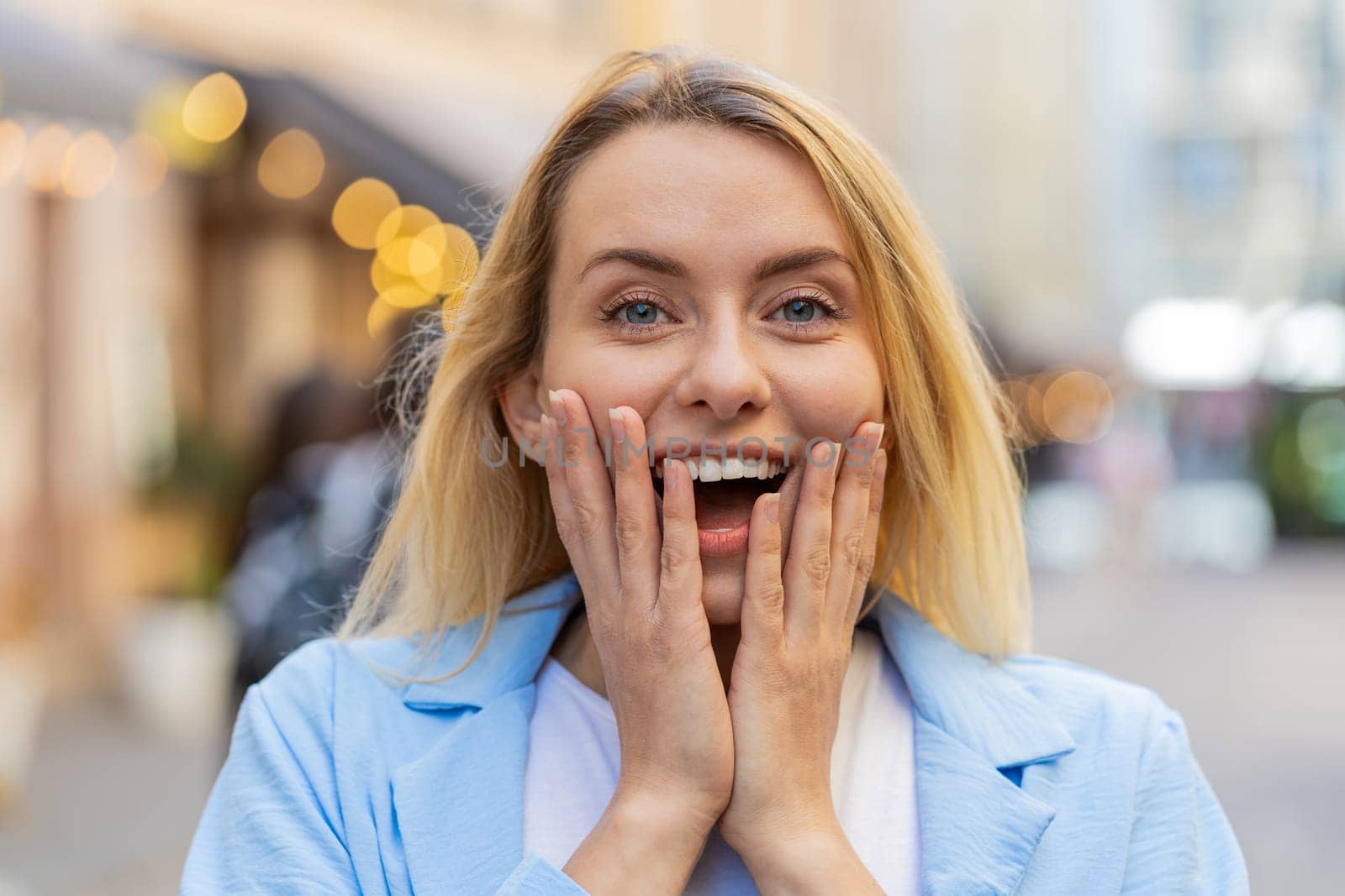 Oh my God, wow. Caucasian young woman looking surprised at camera with big open eyes shocked by sudden victory, game winning, lottery goal achievement, good news outdoors. Lady on city sunshine street