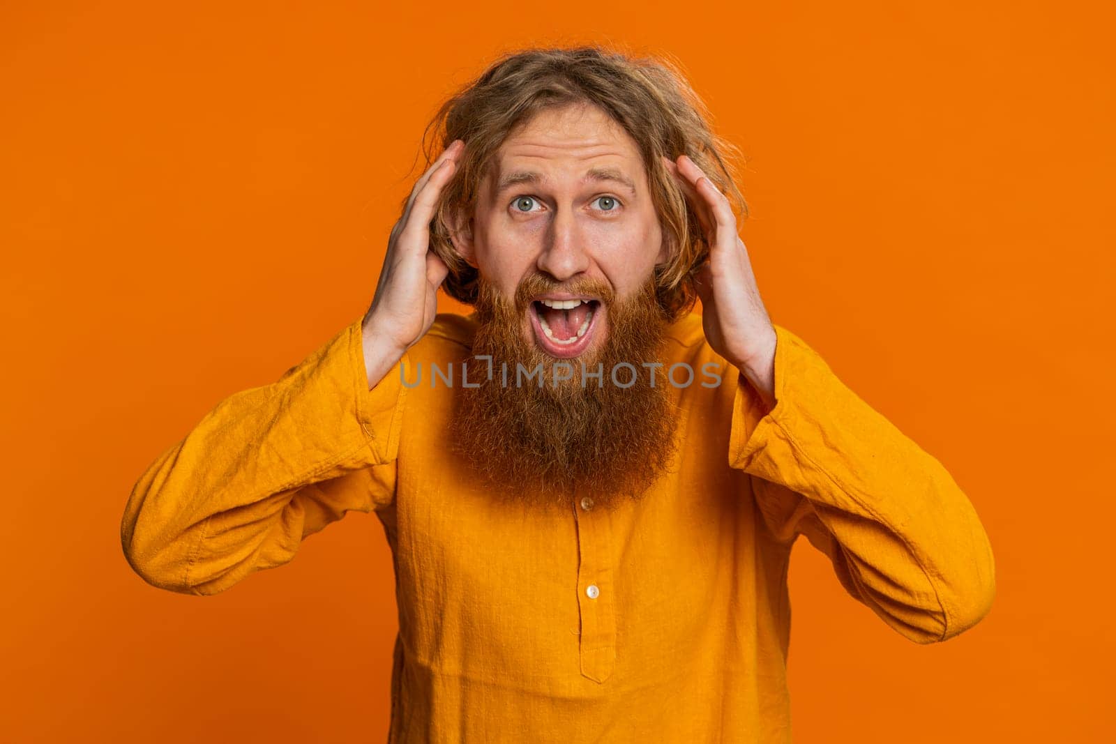 Happy joyful Caucasian man celebrating success victory, winning birthday, lottery jackpot goal achievement play game good positive news triumph. Young bearded guy isolated on orange studio background