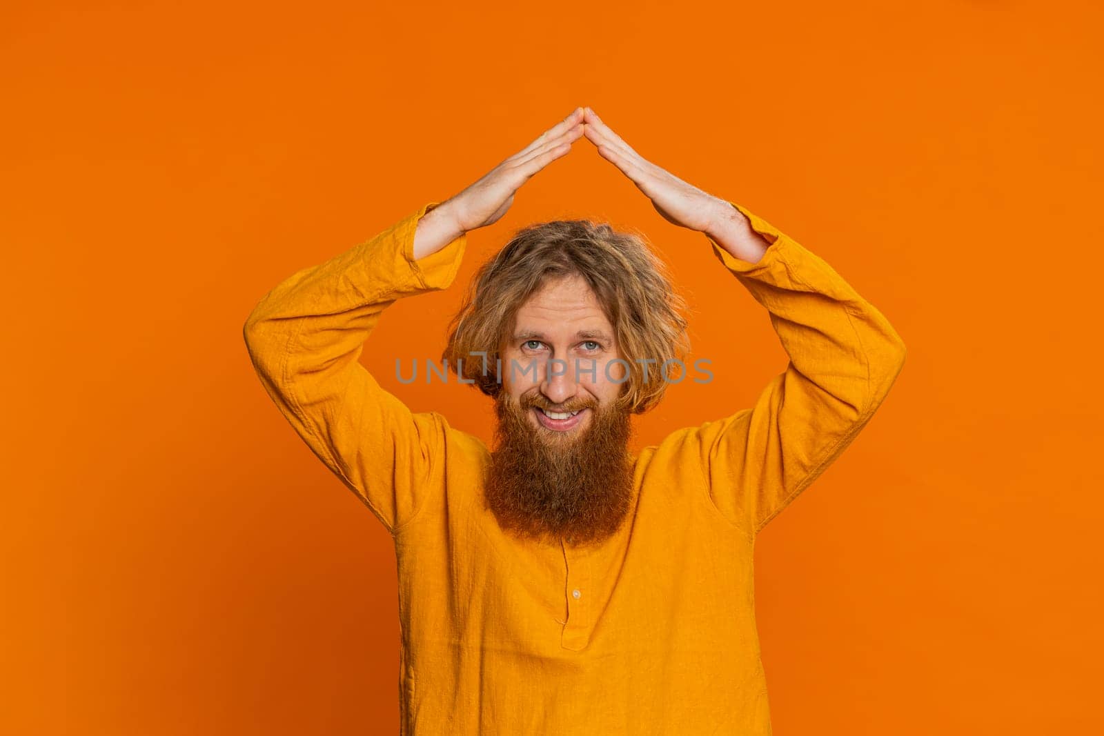 House roof about head. Caucasian man playing childish catching up game, feeling in safe making roof above head with hands, insurance, security service. Redhead young guy isolated on orange background