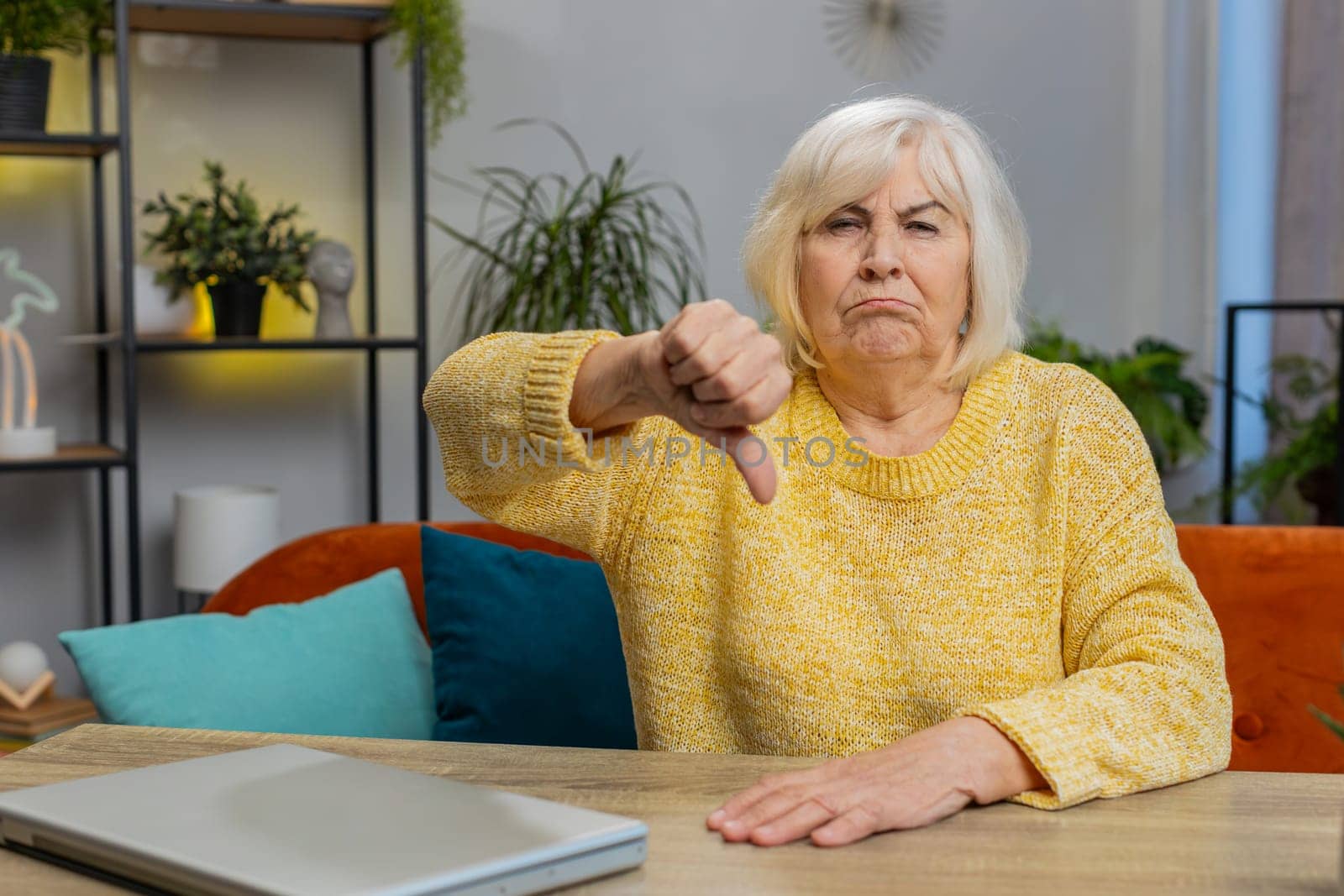 Dislike. Upset unhappy senior woman showing thumbs down sign gesture, expressing discontent, disapproval dissatisfied bad work at home apartment indoors. Displeased elderly grandmother sits at table