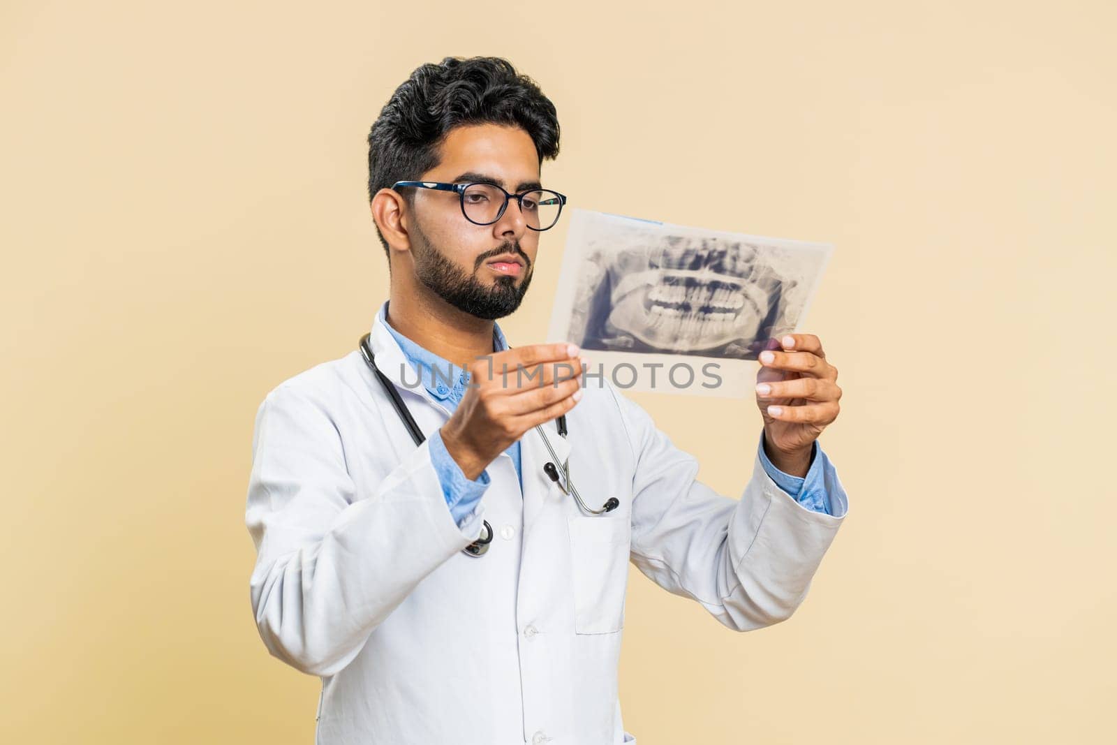 Indian young doctor orthodontist man examines a panoramic x-ray picture of the jaw teeth. 3D model of the patient's mouth, MRI scan. Dentistry, oral care. Arabian stomatology guy on beige background