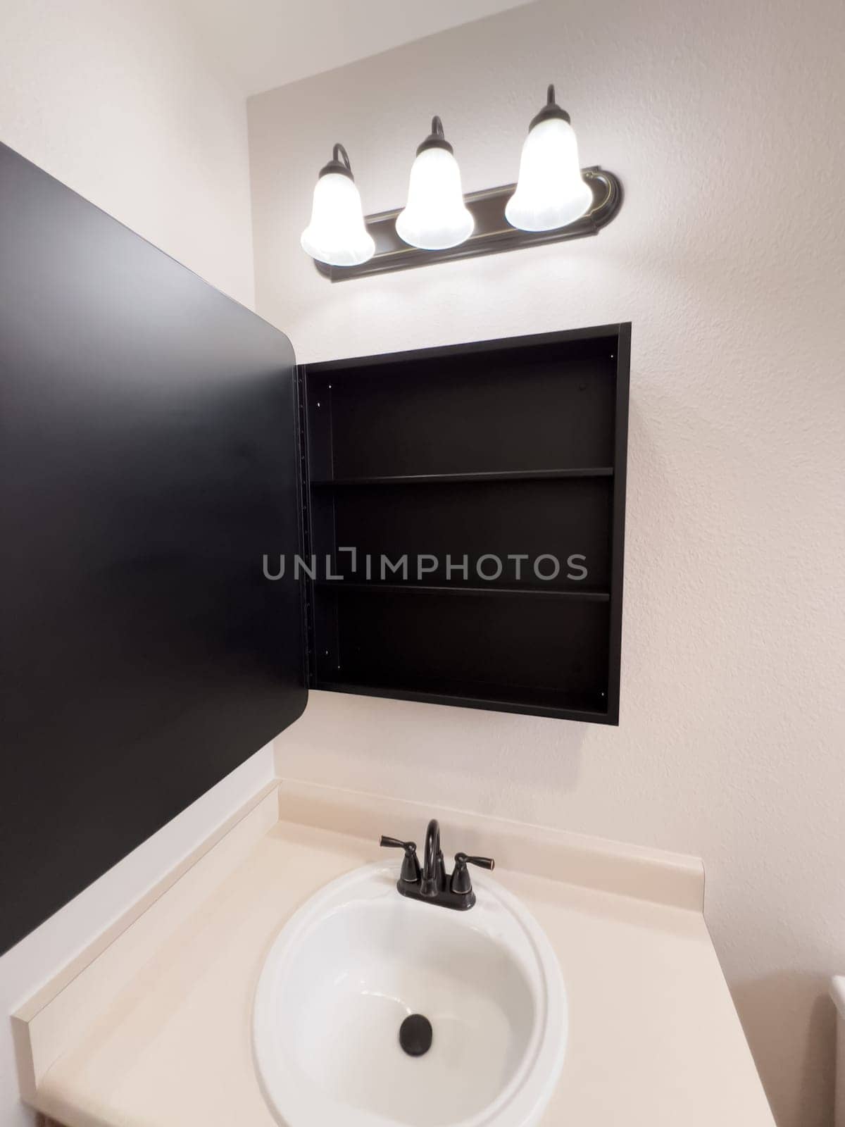 Broomfield, Colorado, USA-January 25, 2025-A stylish bathroom vanity featuring a large rectangular mirror with a black frame, a white sink with a black faucet, and a beige countertop. The vanity is complemented by a three-light fixture above the mirror, providing ample lighting. A black towel bar is mounted on the wall, enhancing the modern design. The bathroom has a clean, minimalist look with neutral tones and functional elements.