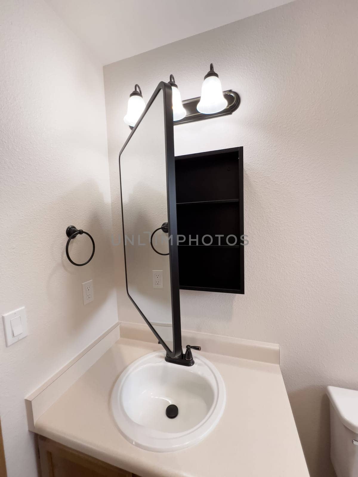 Broomfield, Colorado, USA-January 25, 2025-A stylish bathroom vanity featuring a large rectangular mirror with a black frame, a white sink with a black faucet, and a beige countertop. The vanity is complemented by a three-light fixture above the mirror, providing ample lighting. A black towel bar is mounted on the wall, enhancing the modern design. The bathroom has a clean, minimalist look with neutral tones and functional elements.