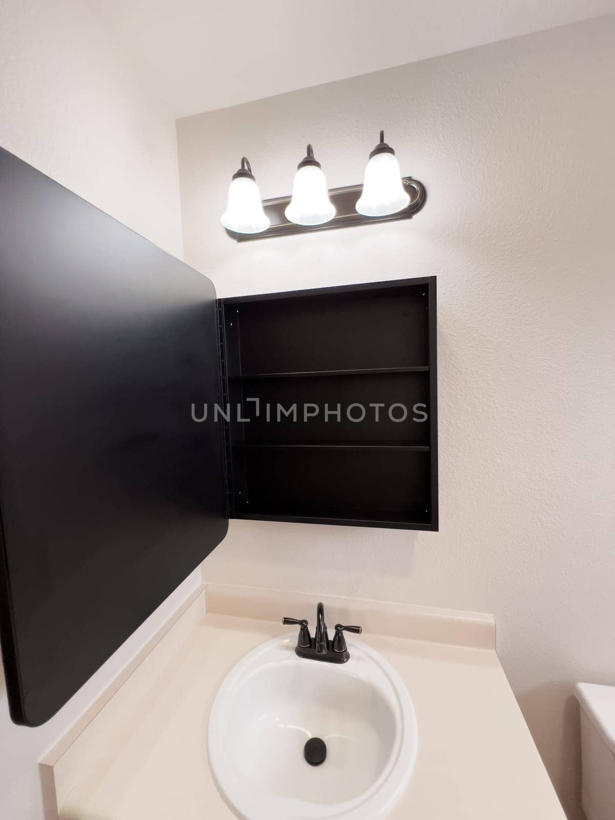 Broomfield, Colorado, USA-January 25, 2025-A stylish bathroom vanity featuring a large rectangular mirror with a black frame, a white sink with a black faucet, and a beige countertop. The vanity is complemented by a three-light fixture above the mirror, providing ample lighting. A black towel bar is mounted on the wall, enhancing the modern design. The bathroom has a clean, minimalist look with neutral tones and functional elements.