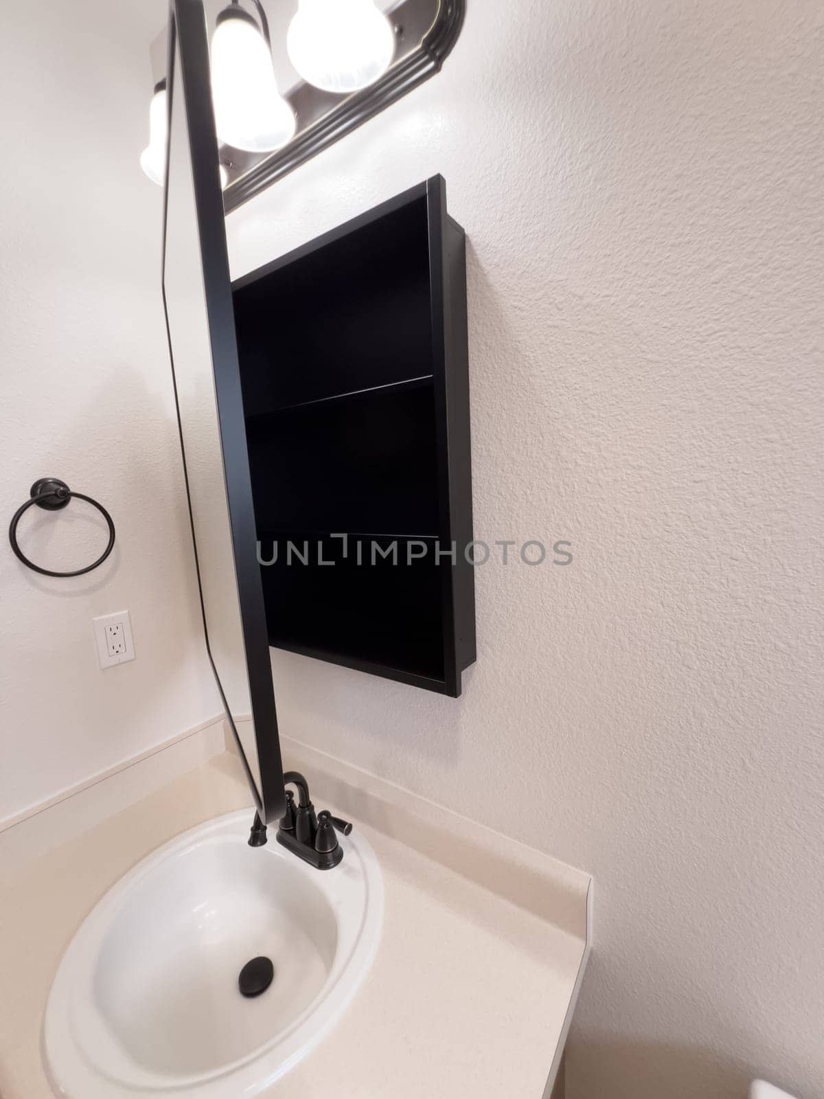Broomfield, Colorado, USA-January 25, 2025-A stylish bathroom vanity featuring a large rectangular mirror with a black frame, a white sink with a black faucet, and a beige countertop. The vanity is complemented by a three-light fixture above the mirror, providing ample lighting. A black towel bar is mounted on the wall, enhancing the modern design. The bathroom has a clean, minimalist look with neutral tones and functional elements.