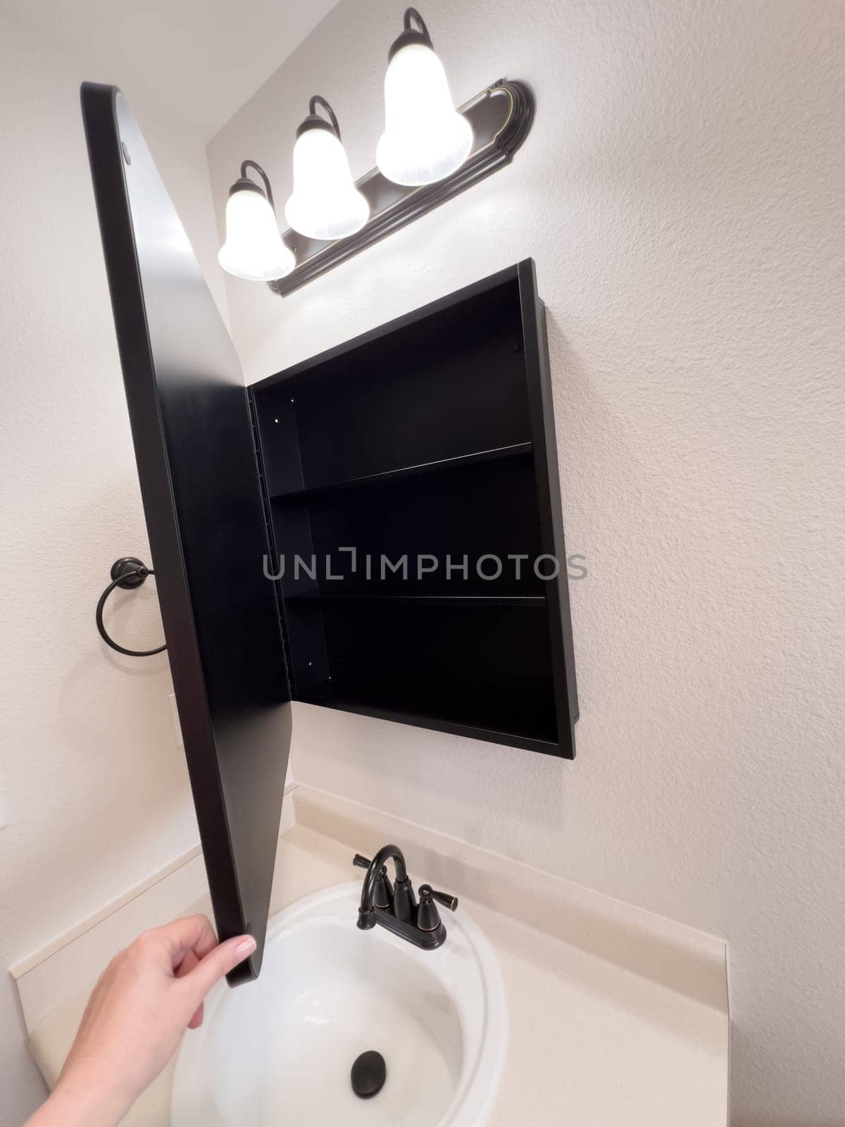 Broomfield, Colorado, USA-January 25, 2025-A stylish bathroom vanity featuring a large rectangular mirror with a black frame, a white sink with a black faucet, and a beige countertop. The vanity is complemented by a three-light fixture above the mirror, providing ample lighting. A black towel bar is mounted on the wall, enhancing the modern design. The bathroom has a clean, minimalist look with neutral tones and functional elements.