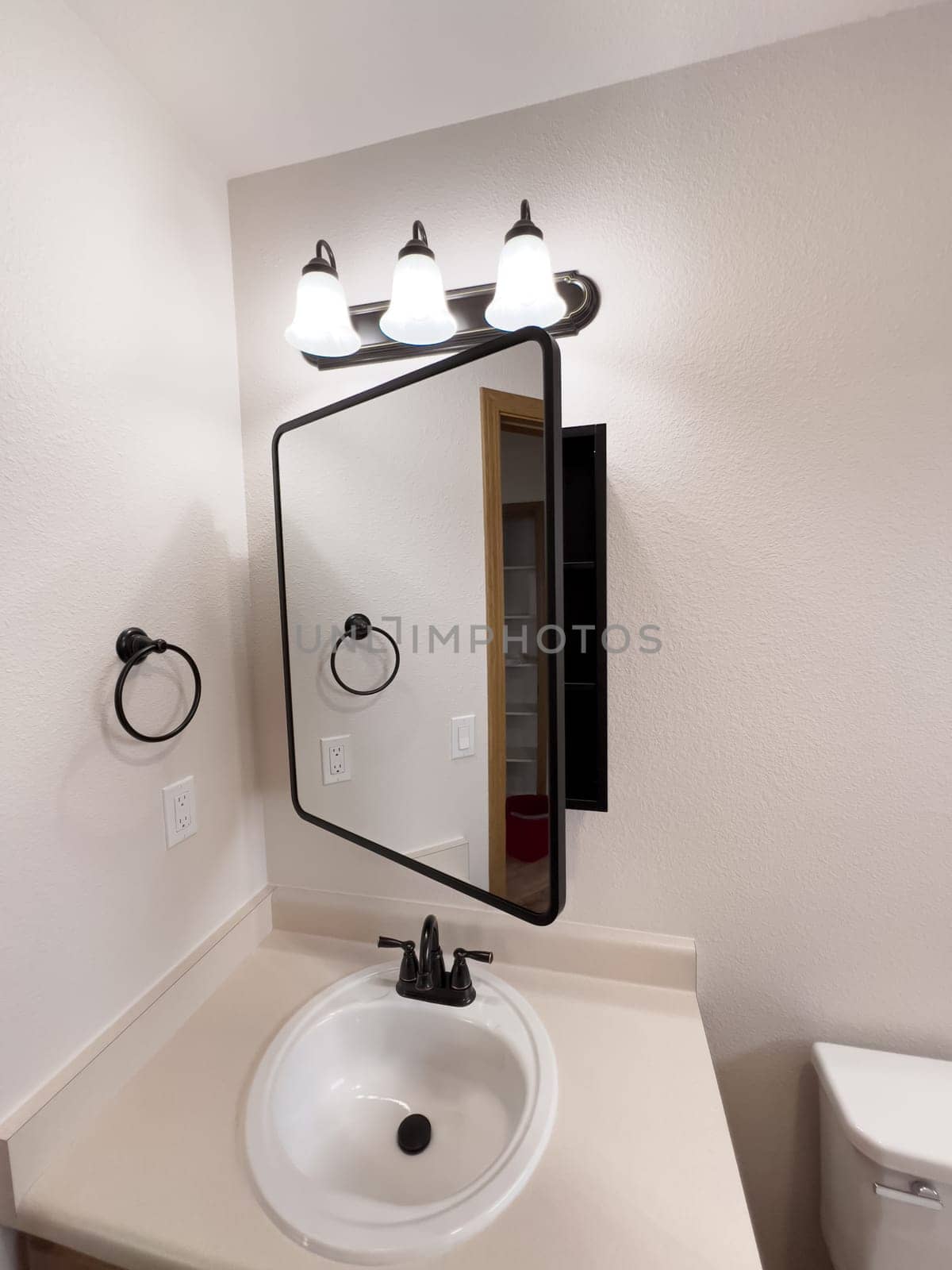 Broomfield, Colorado, USA-January 25, 2025-A stylish bathroom vanity featuring a large rectangular mirror with a black frame, a white sink with a black faucet, and a beige countertop. The vanity is complemented by a three-light fixture above the mirror, providing ample lighting. A black towel bar is mounted on the wall, enhancing the modern design. The bathroom has a clean, minimalist look with neutral tones and functional elements.