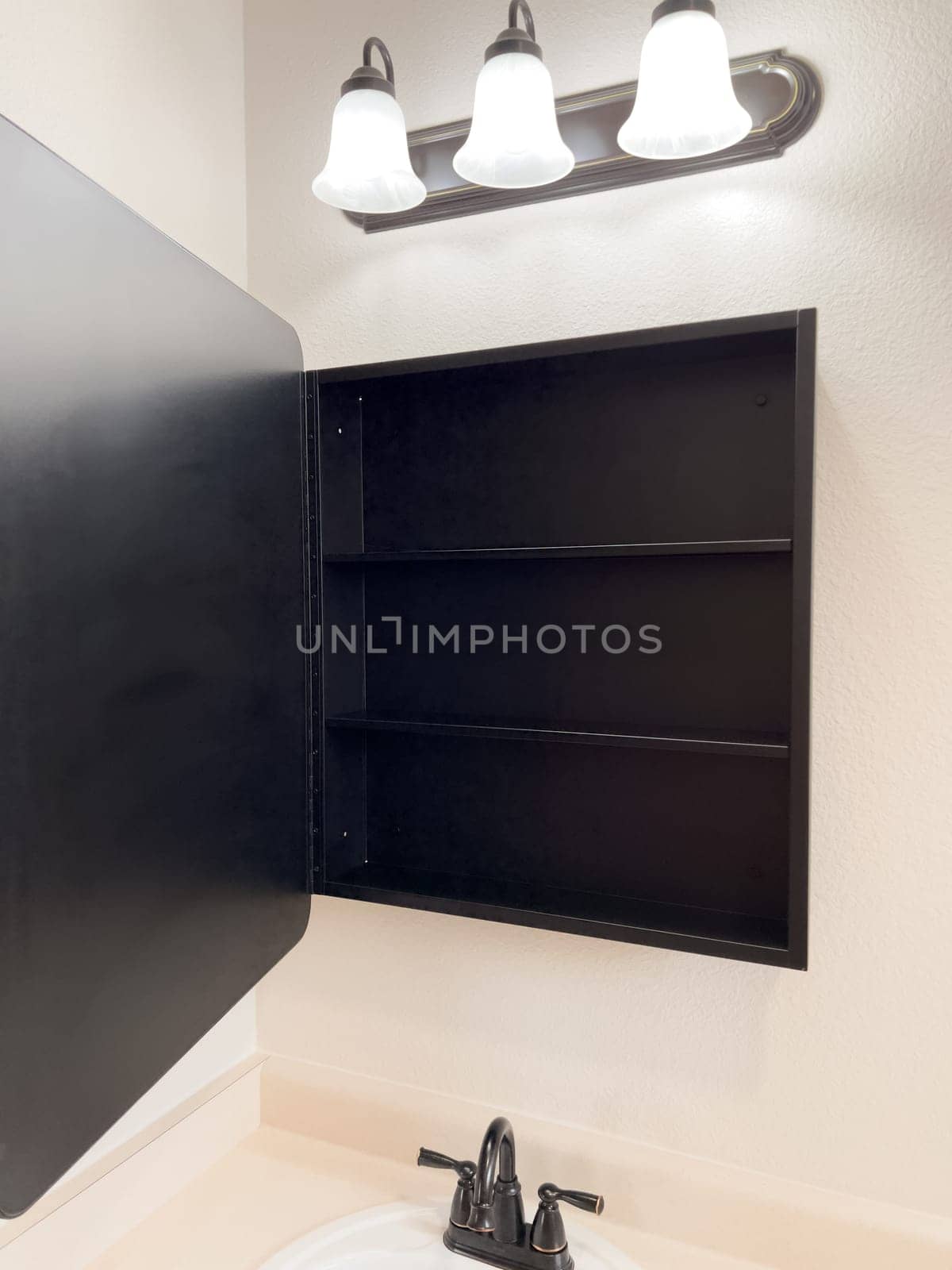 Broomfield, Colorado, USA-January 25, 2025-A stylish bathroom vanity featuring a large rectangular mirror with a black frame, a white sink with a black faucet, and a beige countertop. The vanity is complemented by a three-light fixture above the mirror, providing ample lighting. A black towel bar is mounted on the wall, enhancing the modern design. The bathroom has a clean, minimalist look with neutral tones and functional elements.