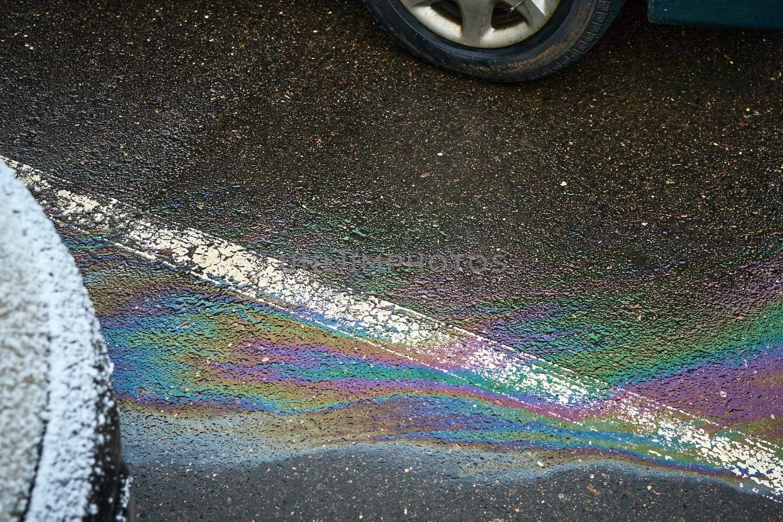 Eye-catching oil slick on wet asphalt by a car, forming a vibrant rainbow sheen that raises awareness about pollution
