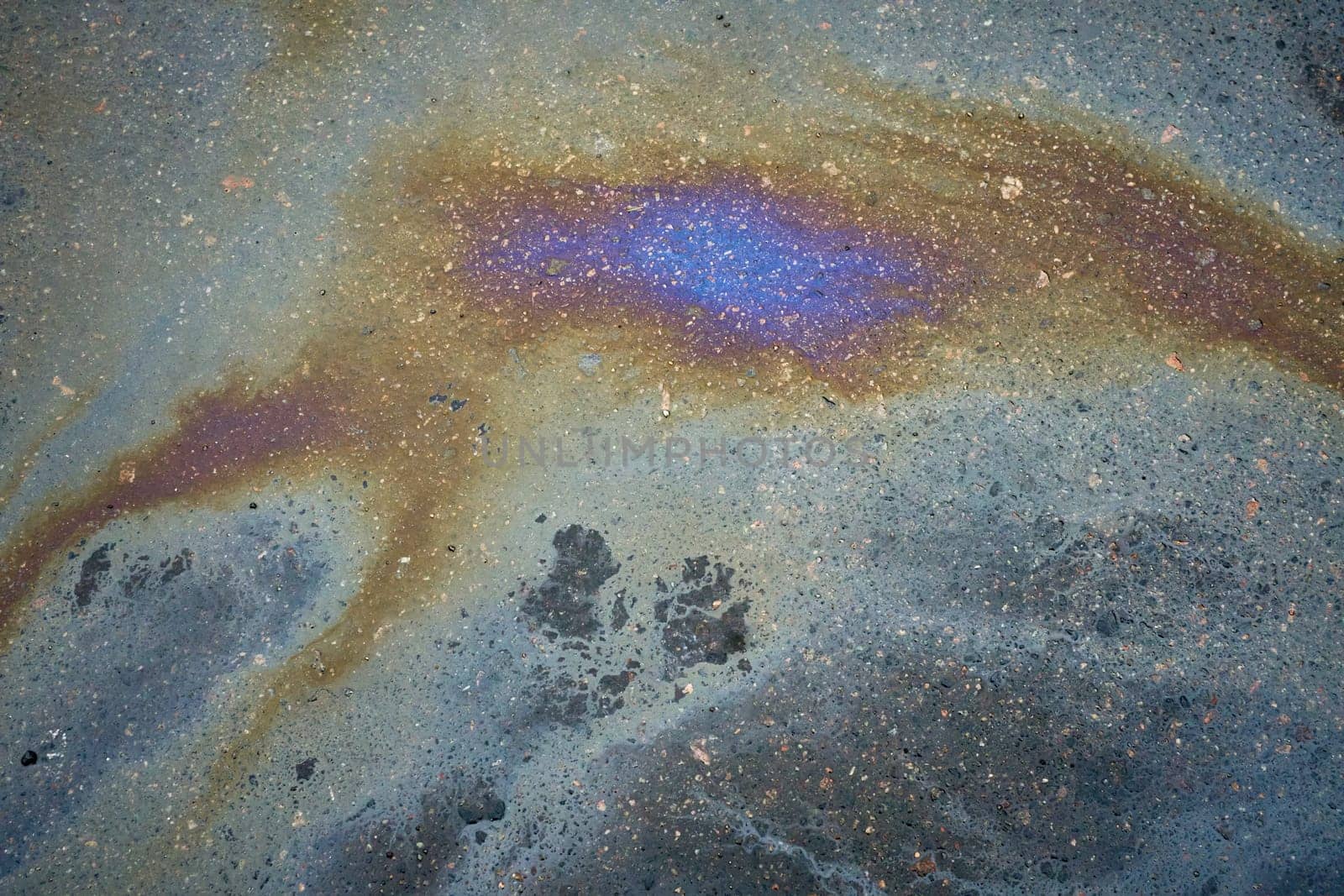 Colorful oil slick reflecting a spectrum of colors on the fissured asphalt road