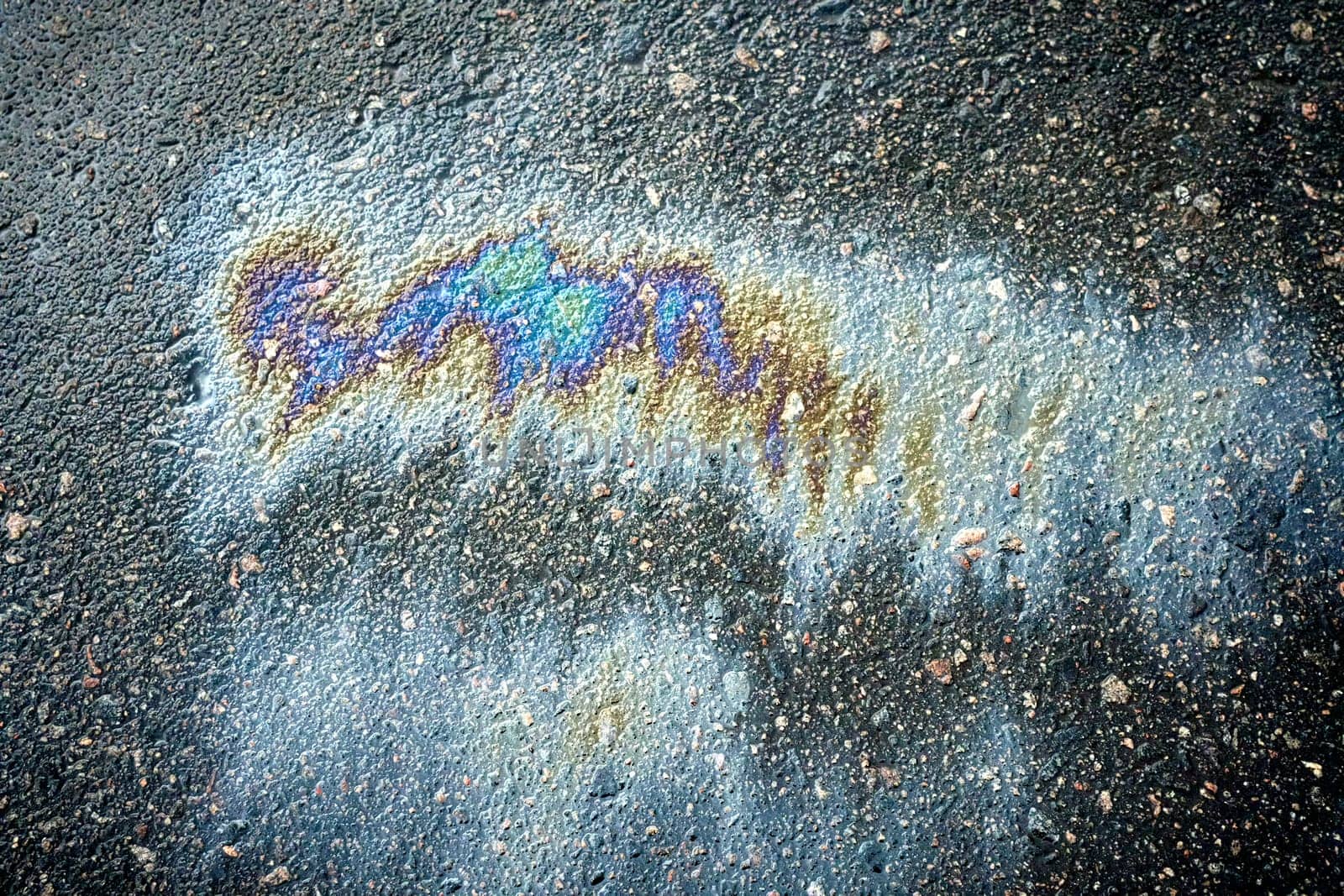 Gasoline or oil spill on asphalt creating rainbow sheen reflecting light