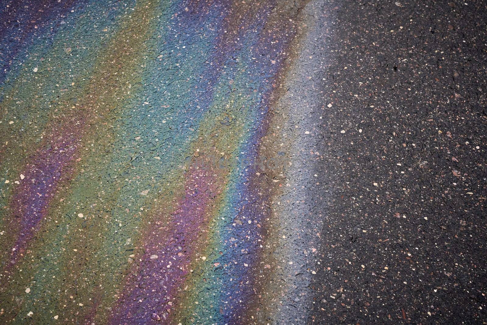 Gasoline or oil spill creating rainbow sheen on asphalt road surface.