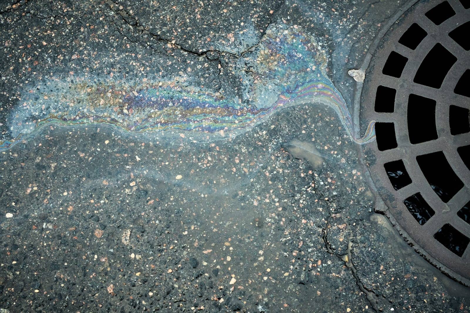 Iridescent gasoline polluting street flowing towards storm drain, environmental damage