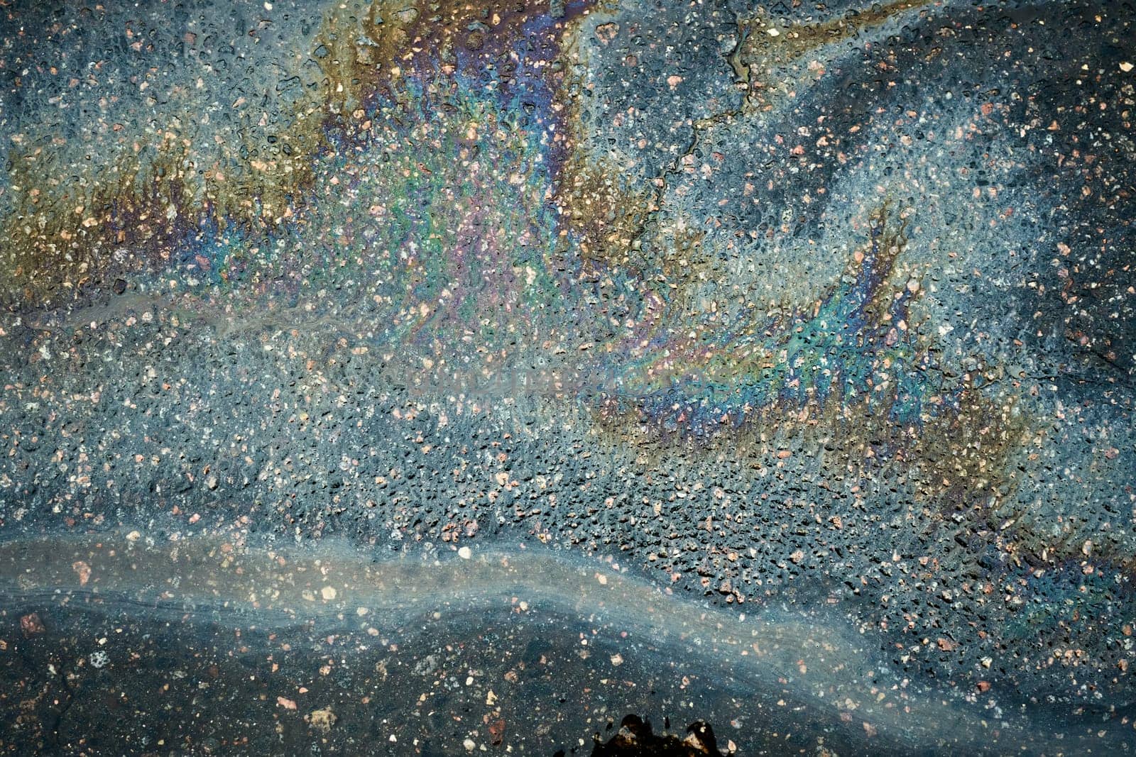 Gasoline rainbow sheen flows towards storm drain on asphalt