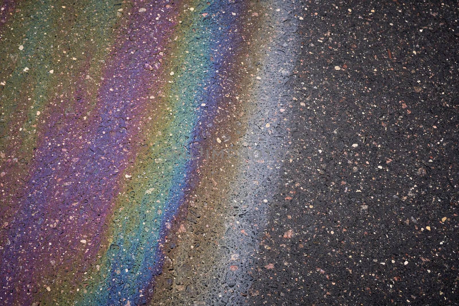 Gasoline spill creating rainbow sheen on asphalt road surface