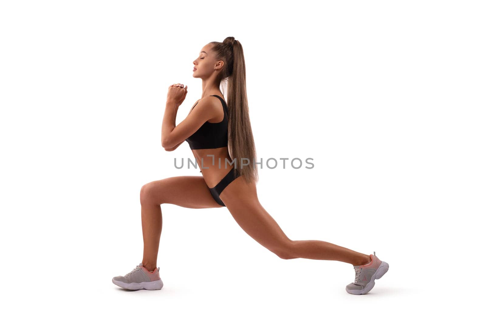 Side view of sexy slender female in sports bra and sneakers exercising on white background in studio and looking away isolated