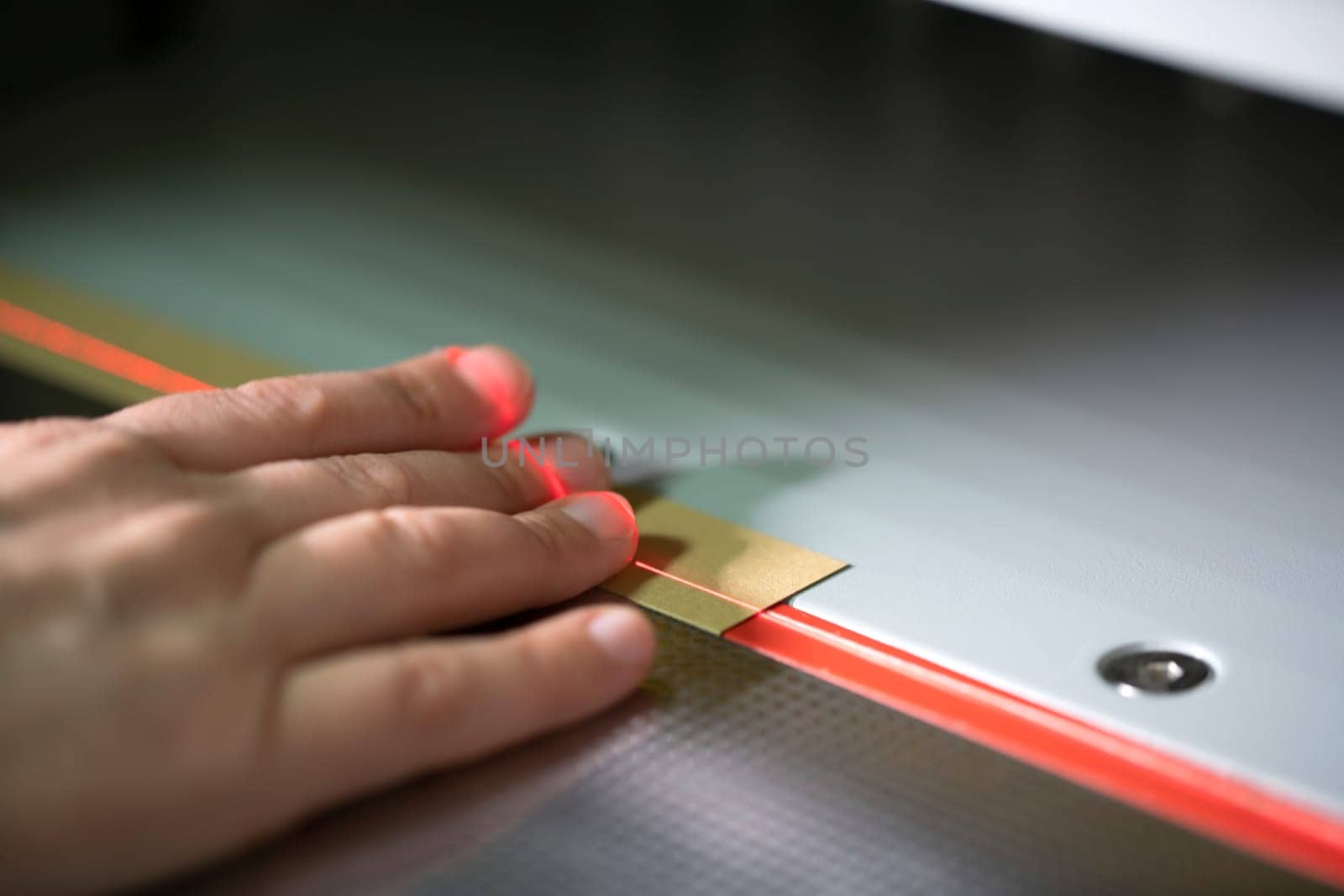 Crop unrecognizable female fingers on laser line of modern digital paper cutting machine in workshop