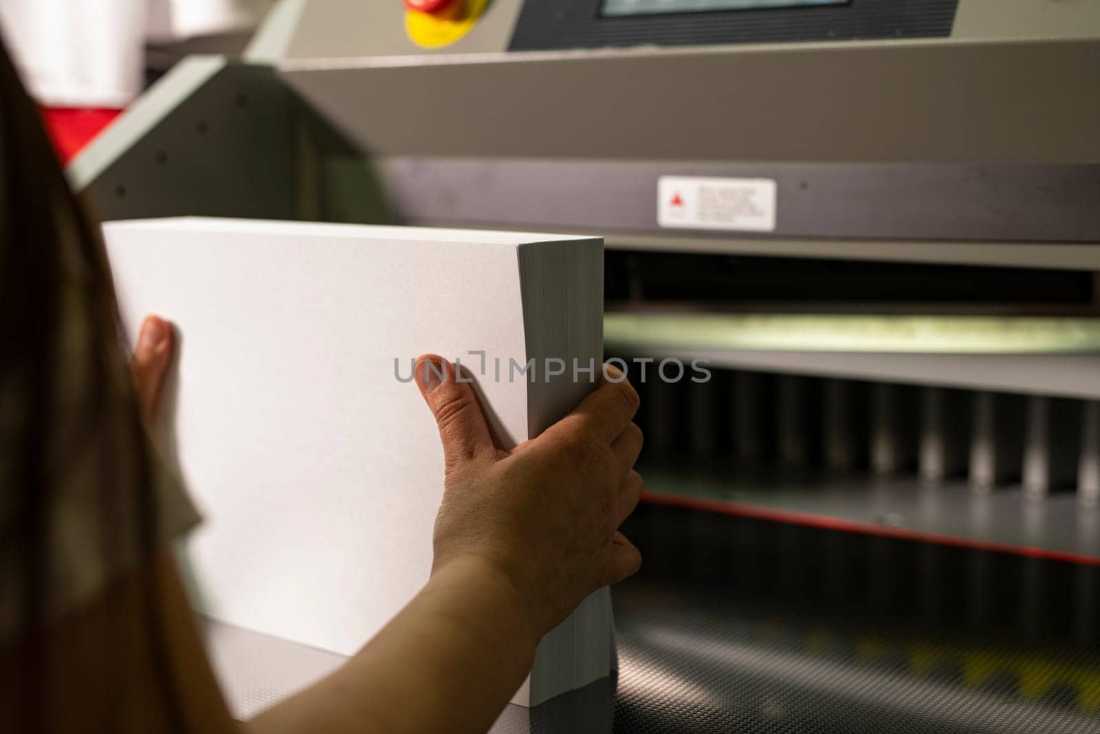 Woman hands prepare pack of paper for cutting on special equipment for production notepads with laser line and metal details