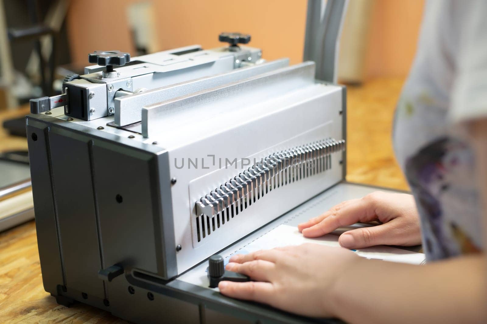 Crop unrecognizable female employee using manual bookbinder machine while creating new notebook in workshop
