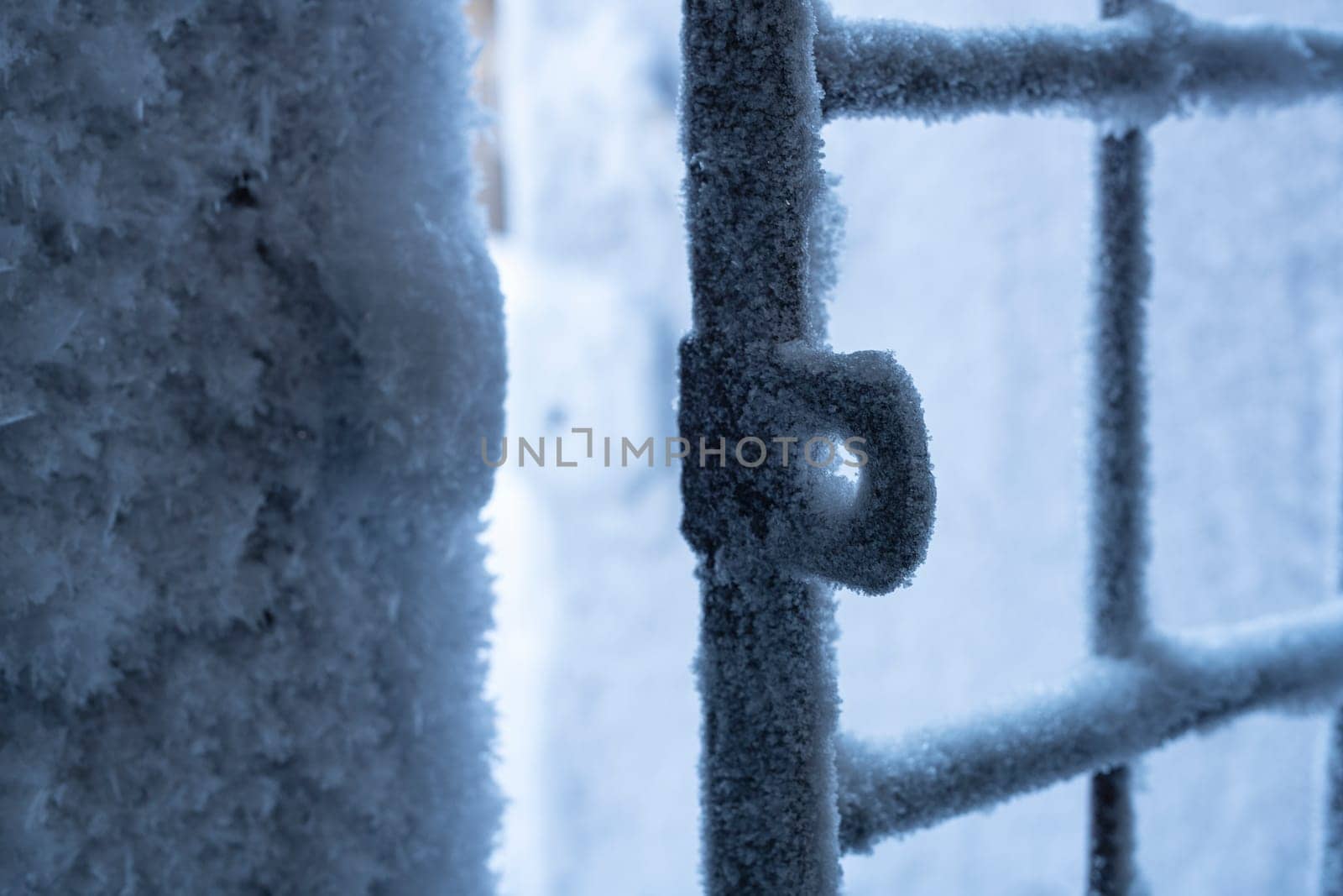 Closeup of open metal grating fence covered by white hoarfrost in cold winter day