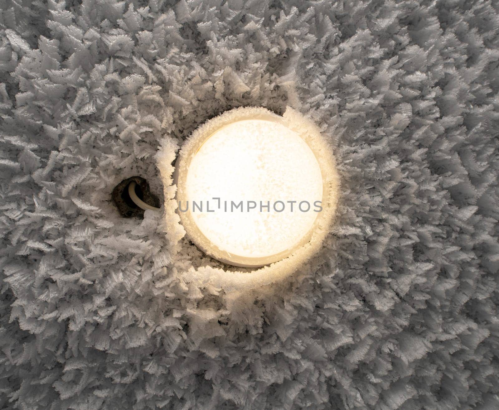 Closeup of round shaped lamp shining on frozen ceiling covered with white hoarfrost in frozen wintertime