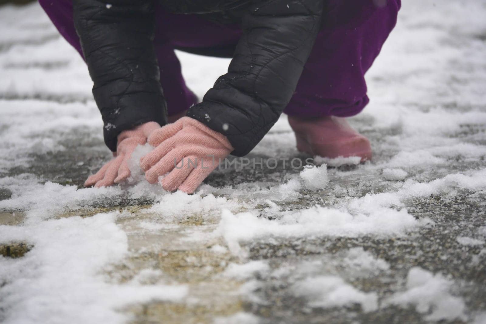 Child kneels in snow, using gloved hands to touch the cold surface.