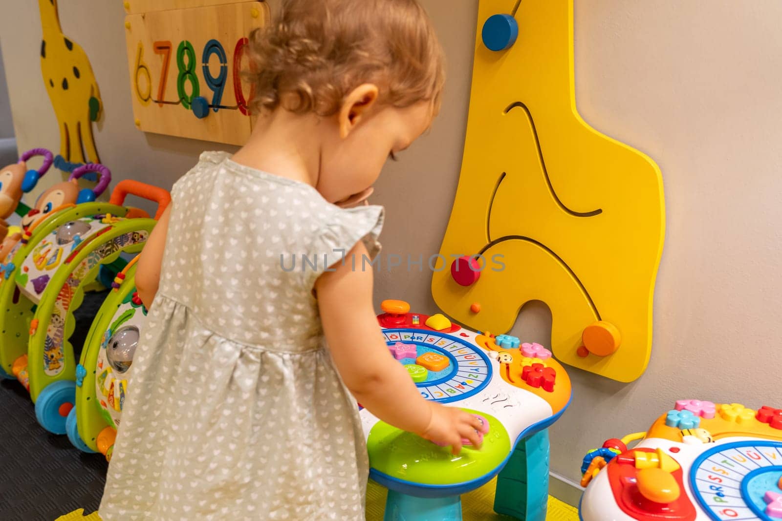 Toddler enjoying a vibrant playroom filled with colorful toys and an educational activity table. Concept of interactive play and fostering childhood development through fun learning experiences
