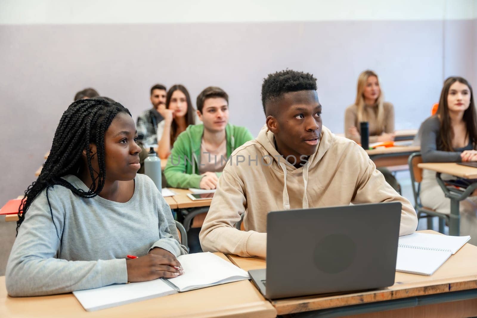 Multi ethnic students listening to lesson in university classroom, using laptop and taking notes