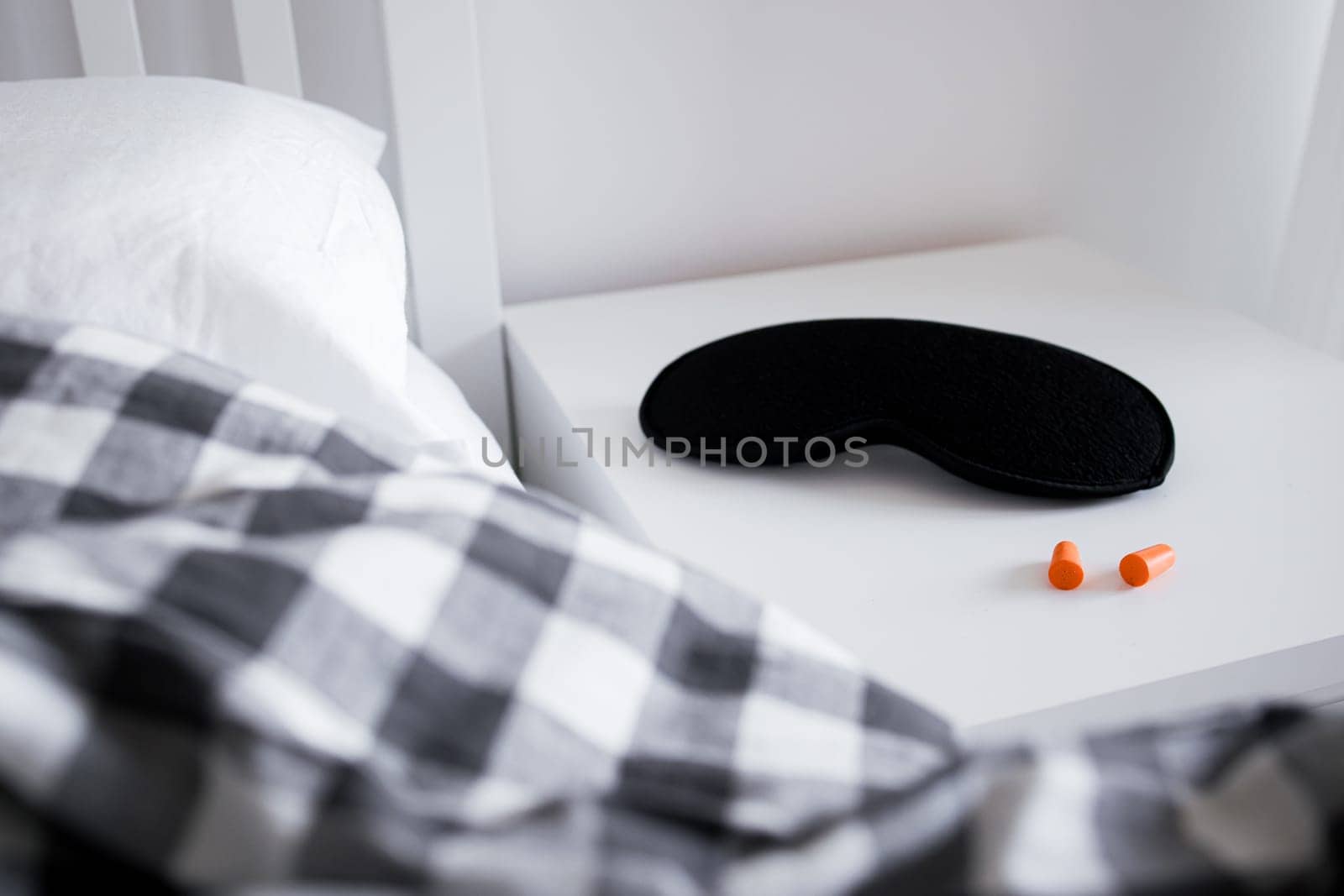 Cozy bedroom with sleep mask and earplugs on nightstand in soft light.