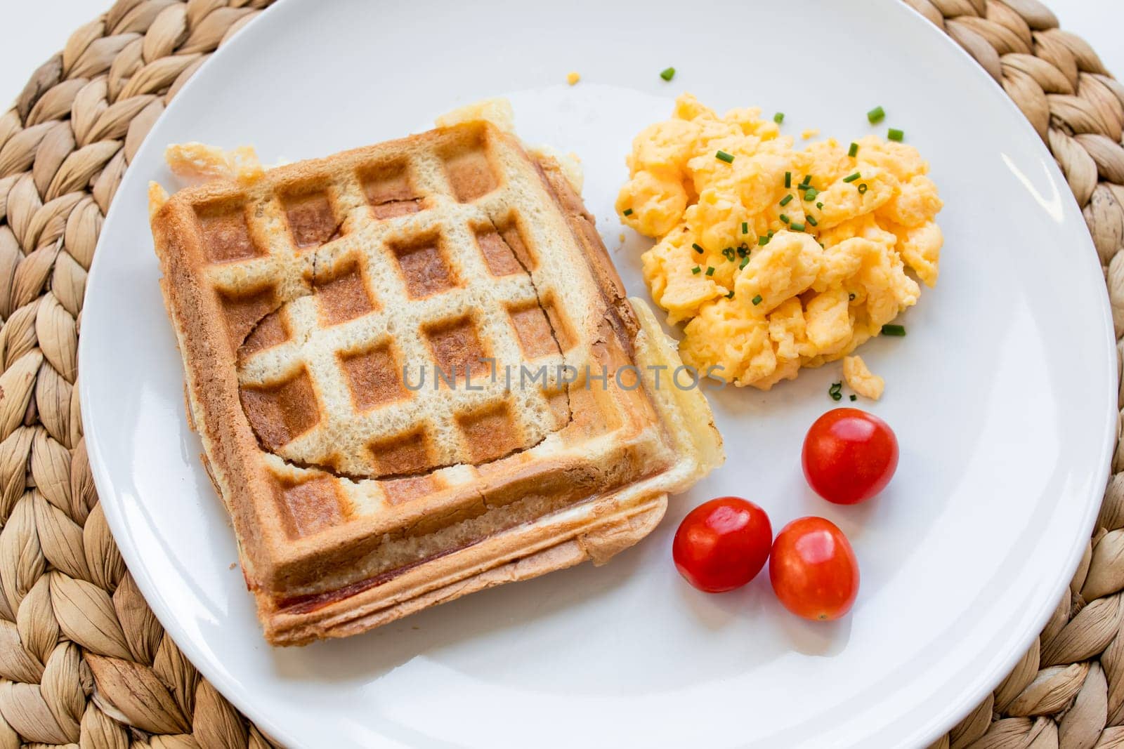 Breakfast plate with ham and cheese toast, scrambled eggs, and tomatoes.