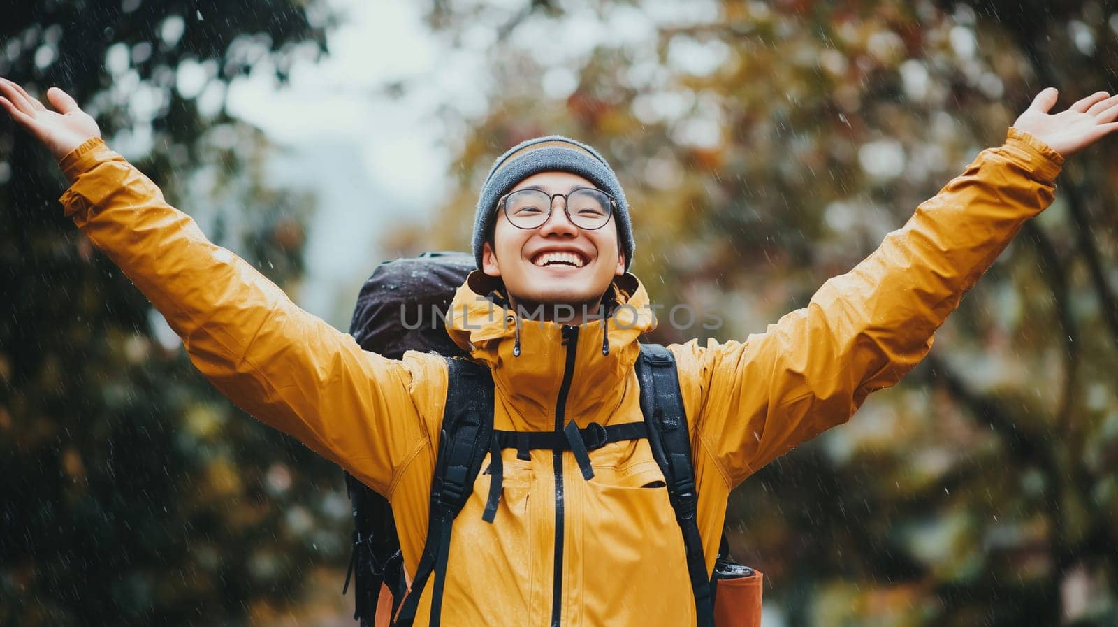 Travel, hiking, adventure, happy joyful young Asian traveler man laughing in yellow jacket enjoying the rain stands in forest, warm day