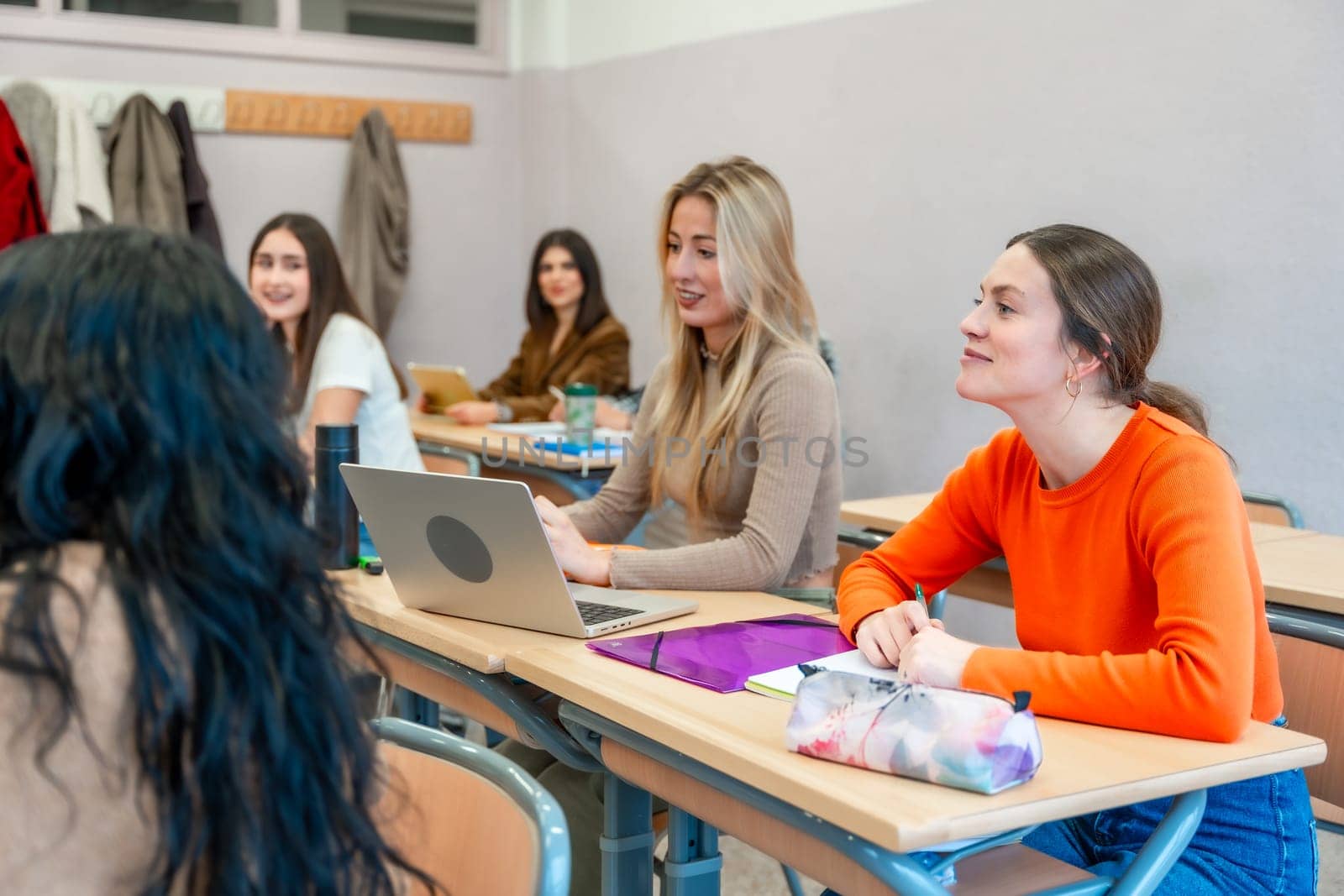 Group of female university students listening attentively to a lecture in a classroom, engaging with the educational material and using a laptop