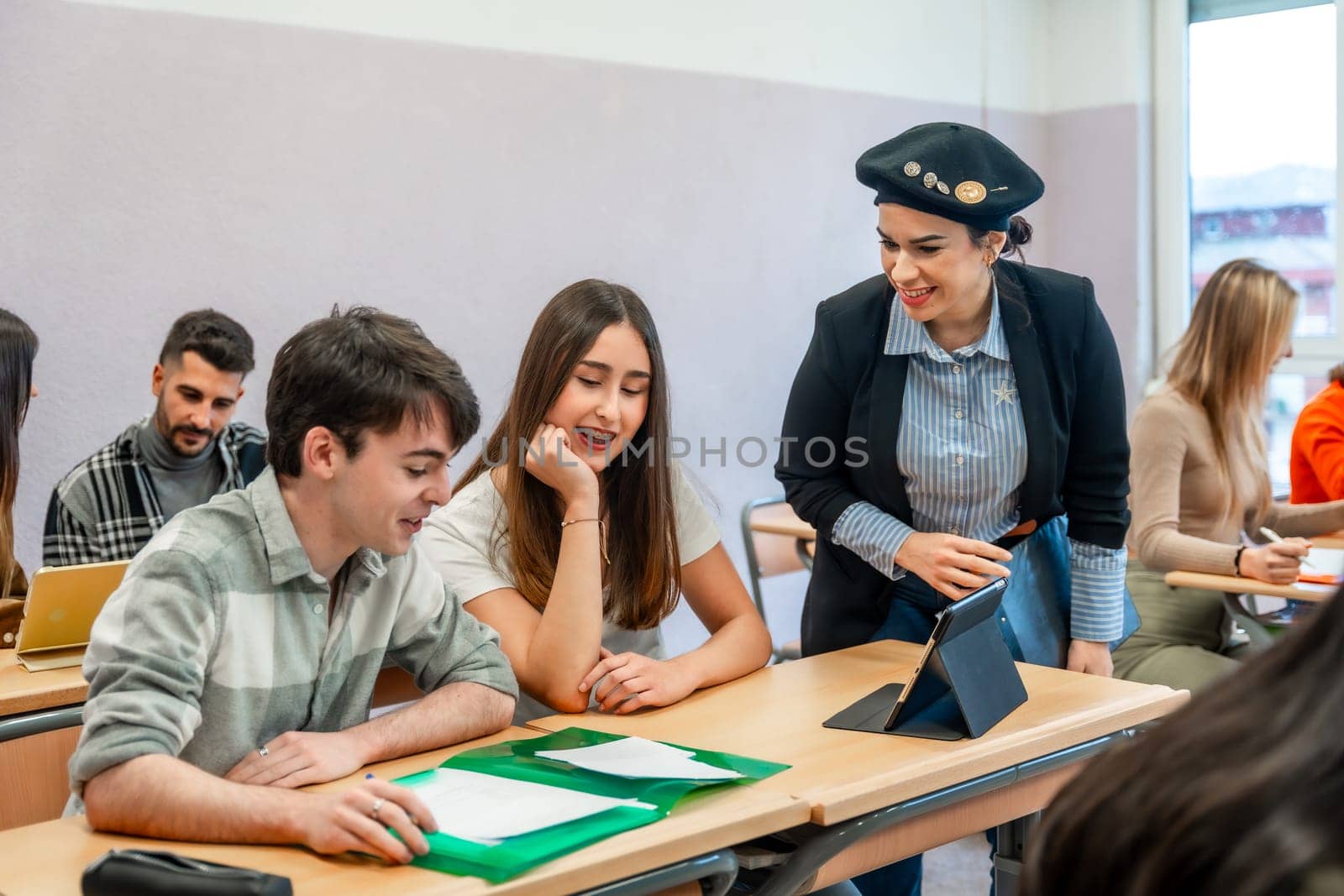University teacher using tablet explaining lesson to two students sitting at desk in classroom