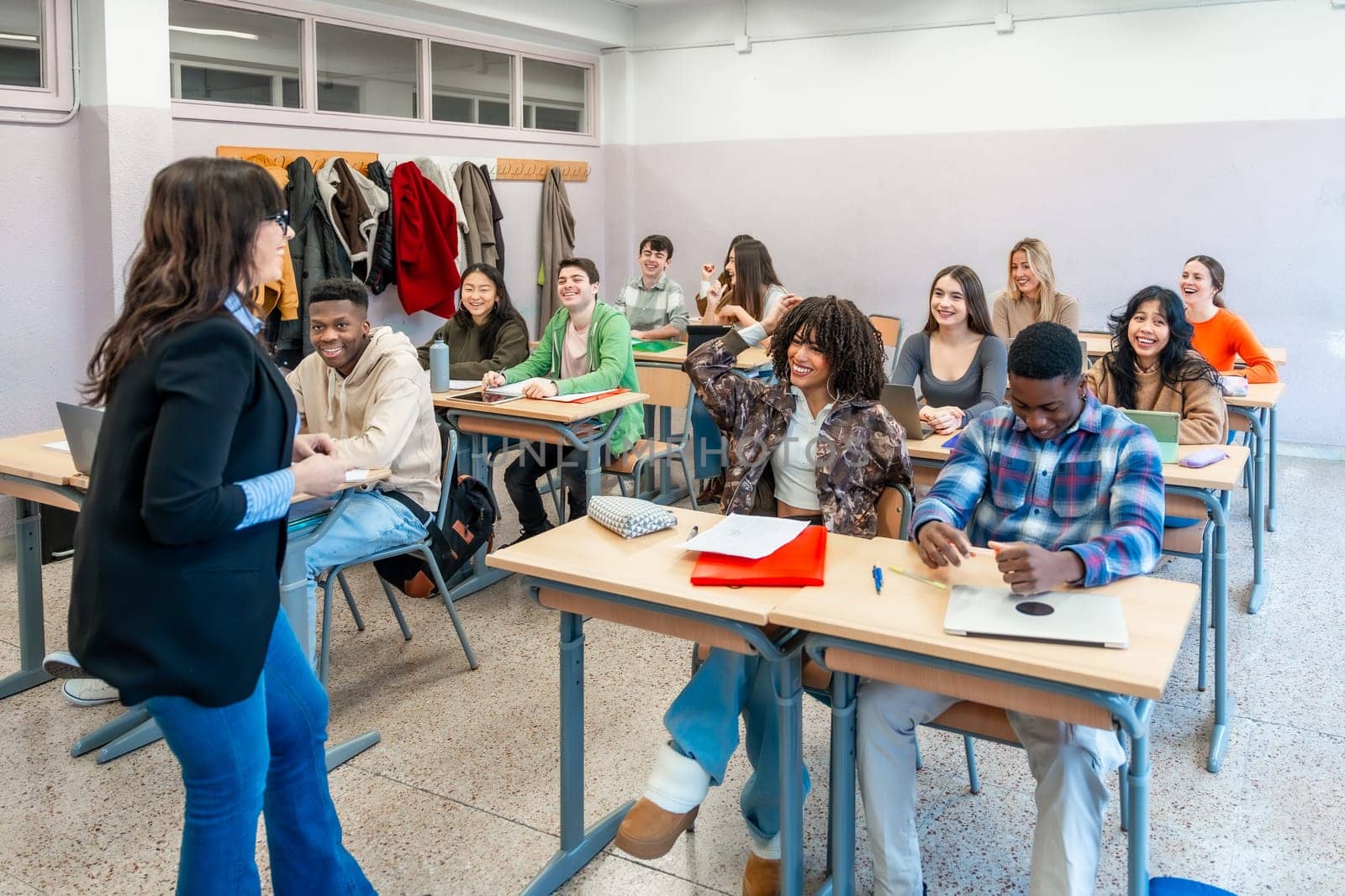 Multi ethnic university students attending a lesson with their professor, participating actively and enjoying learning in a modern classroom