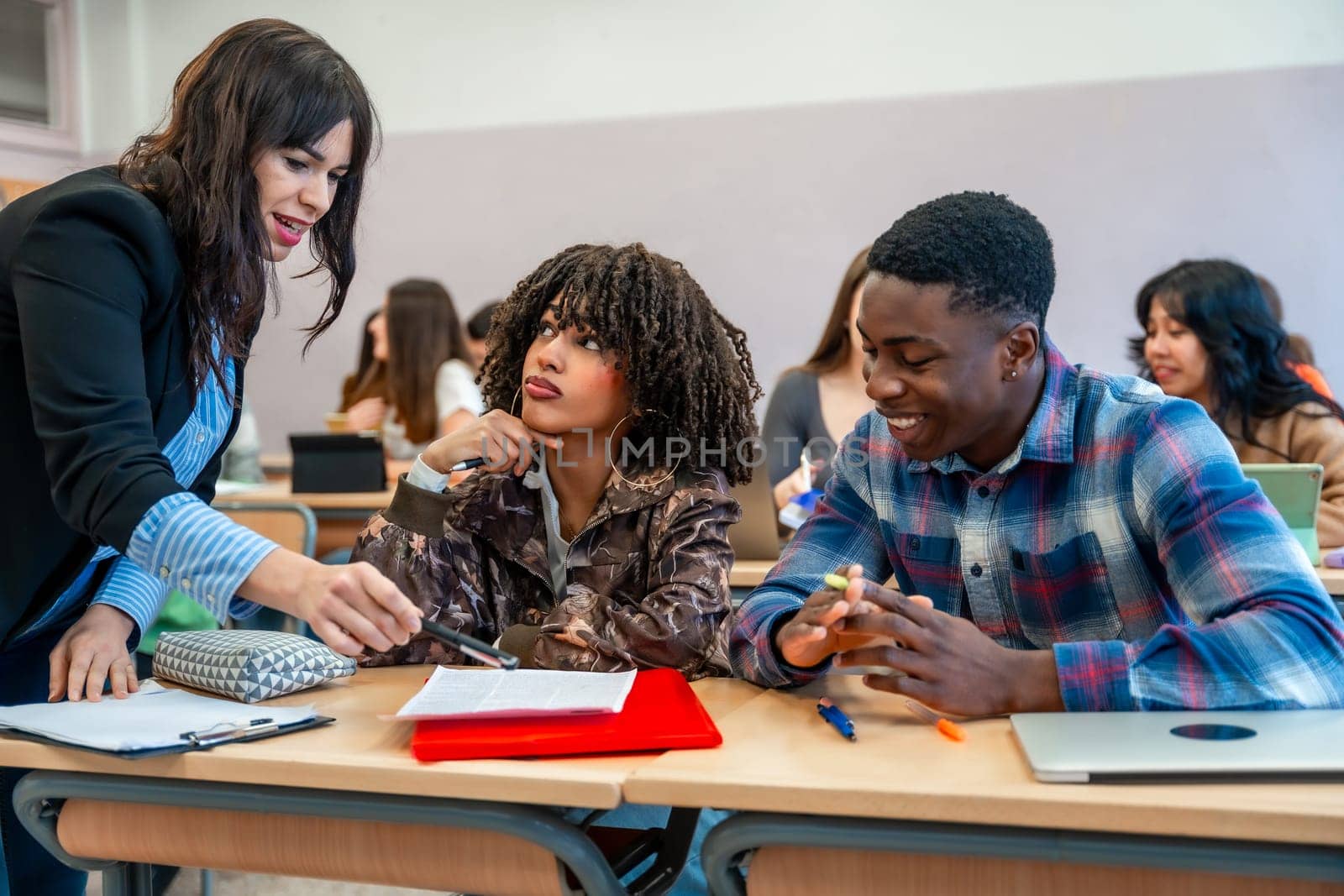 Professor explaining lesson to diverse university students sitting at desk, helping them with their studies