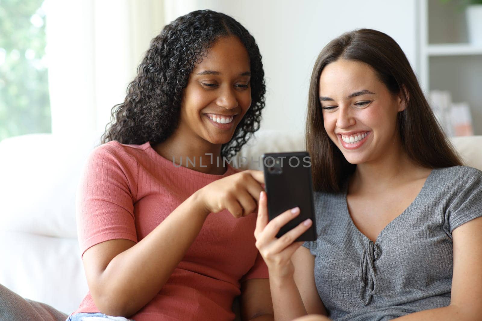 Happy interracial friends checking phone content at home