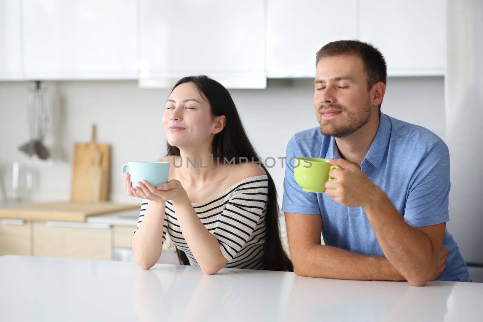 Interracial roommates drinking and breathing in a kitchen at home