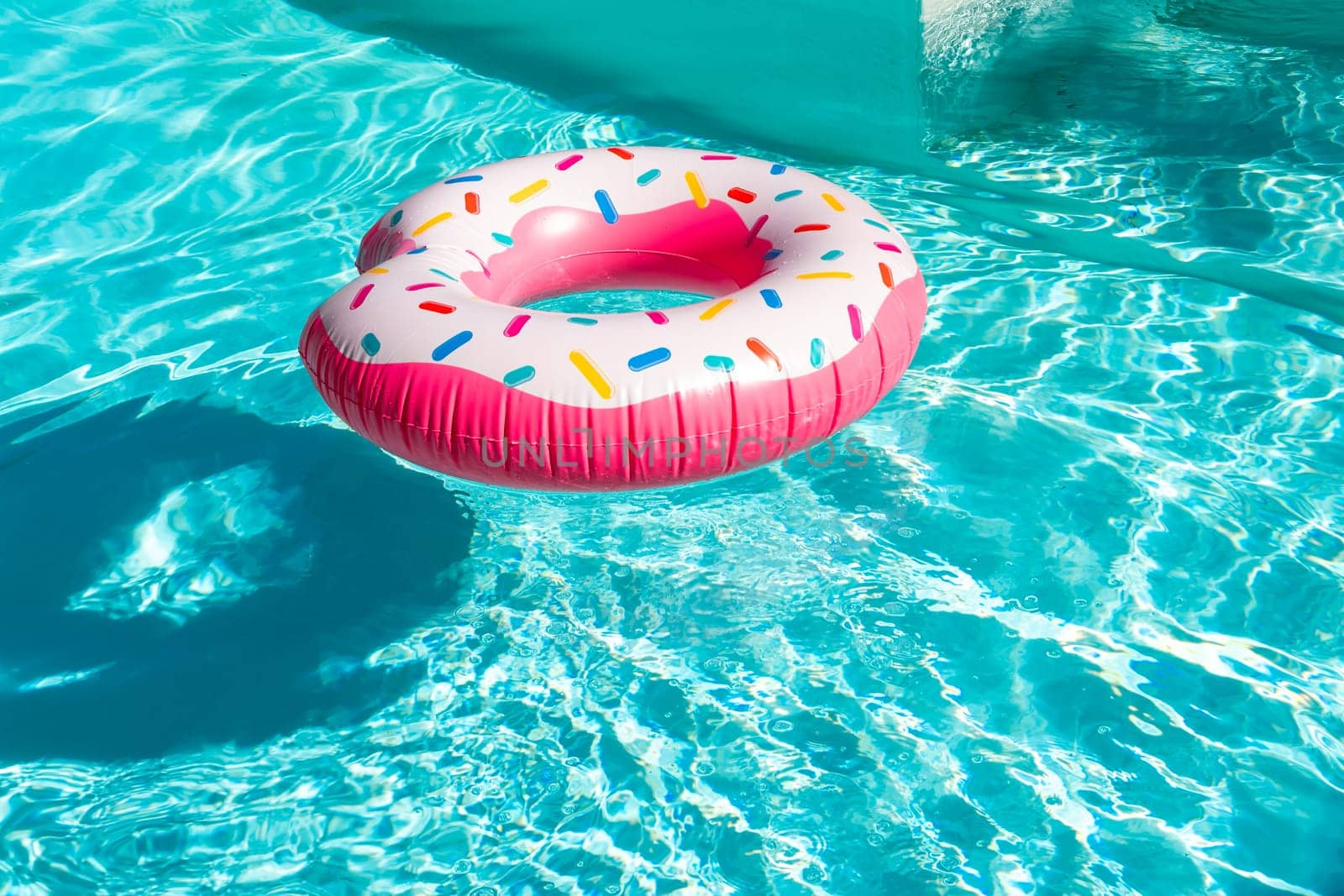Pink donut-shaped inflatable float in turquoise swimming pool with shadow and sunlight reflections