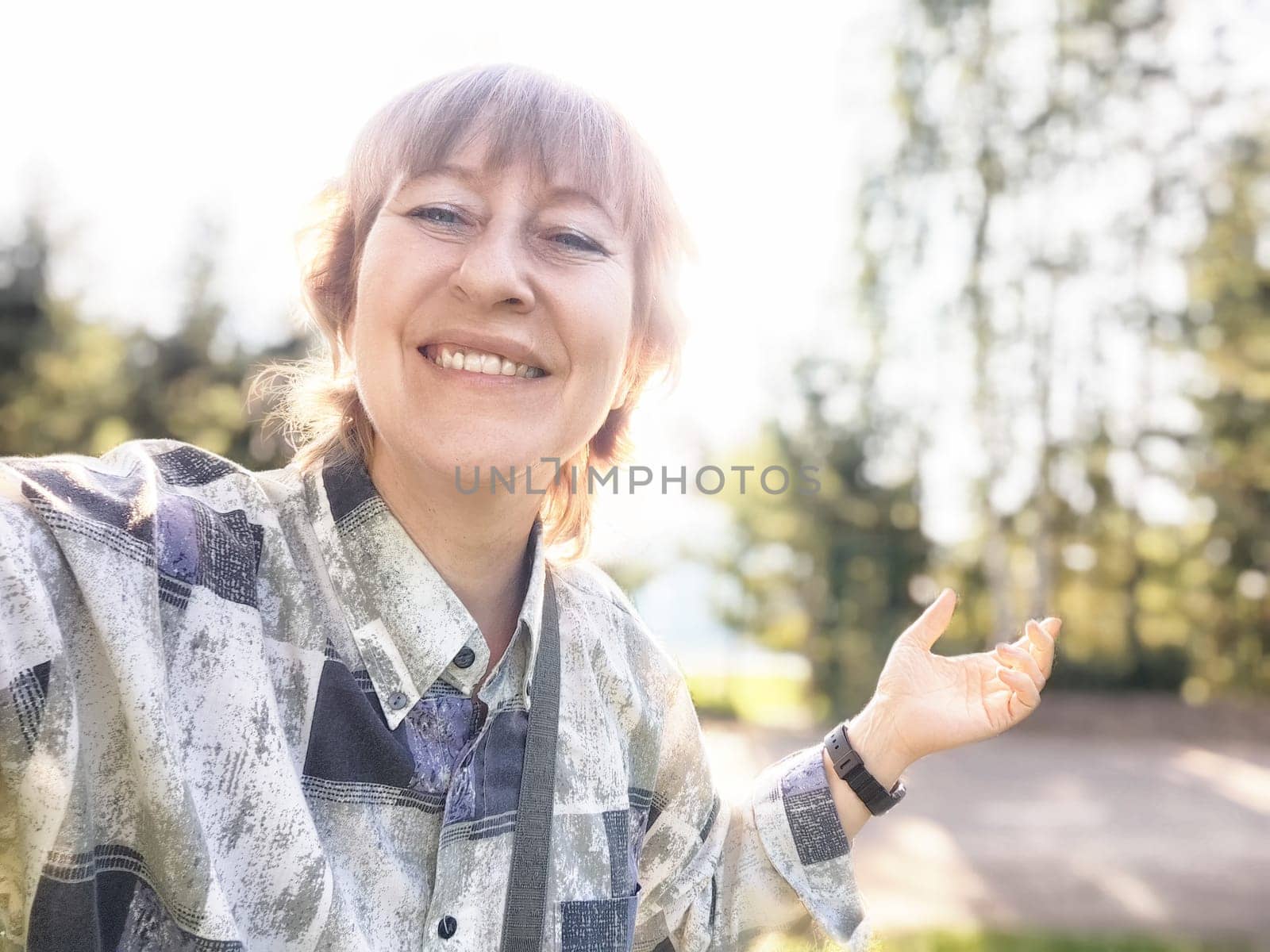 A middle-aged woman smiles as she takes a selfie in a beautiful natural landscape, capturing her travel adventure.