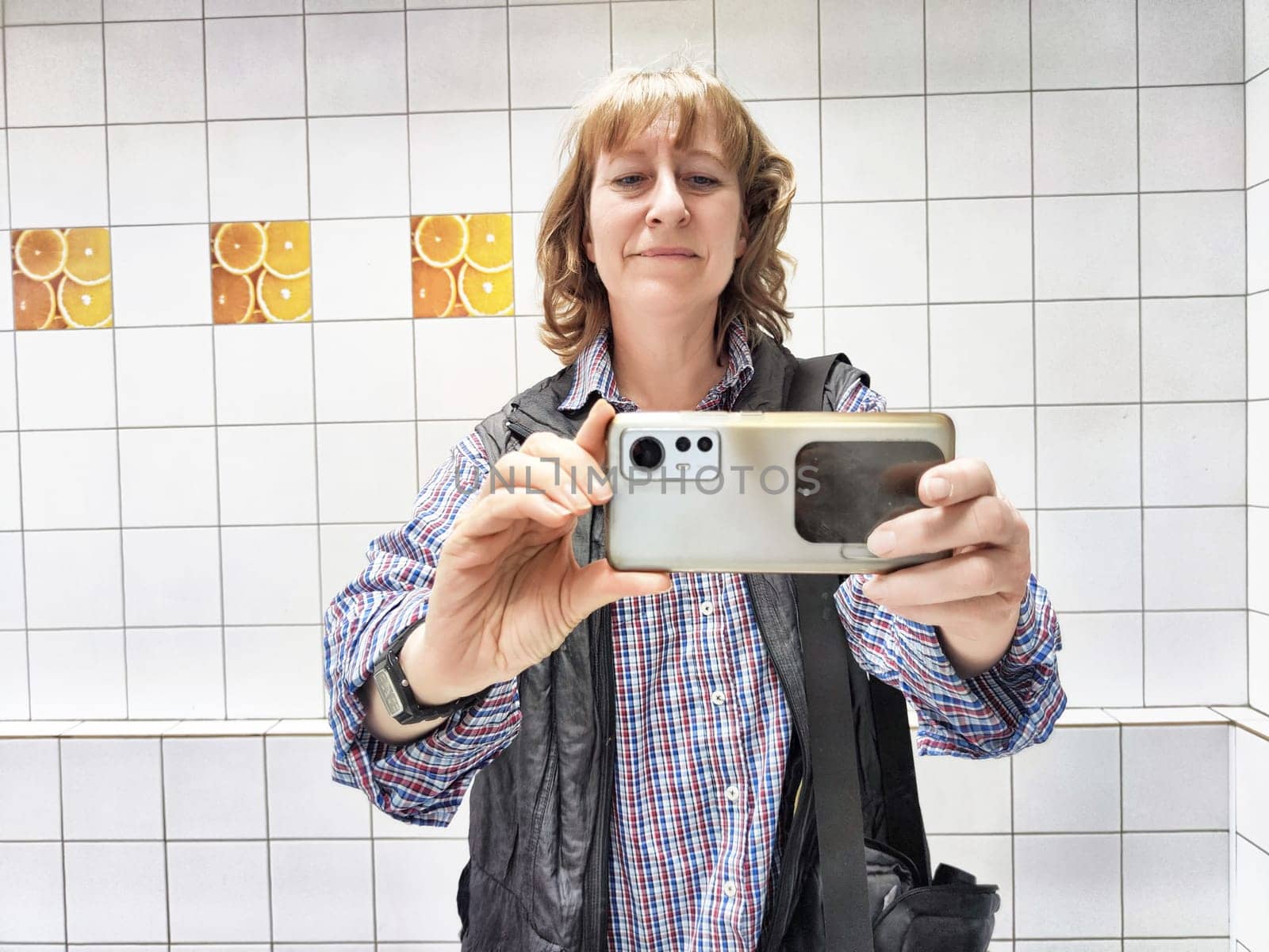 A middle-aged woman with blonde hair captures a selfie in her bright bathroom while enjoying her morning routine.