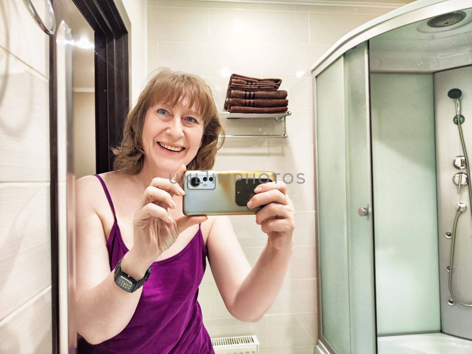 In the early morning light, a middle-aged female blogger enjoys a cheerful moment taking a selfie in her bathroom.