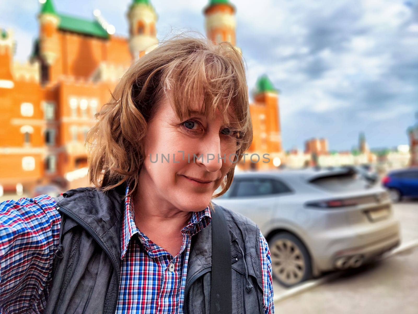 Female traveler blogger takes a cheerful selfie in a bustling city while enjoying her summer trip adventure.