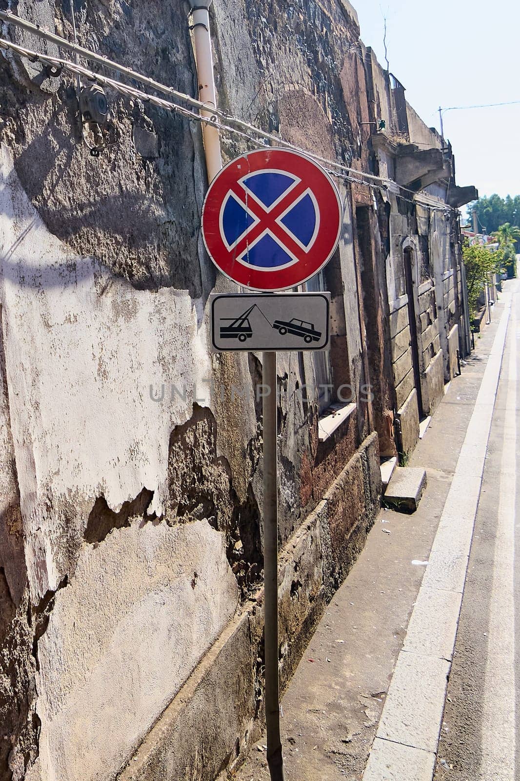 Urban street sign. A no parking and tow-away zone sign on a weathered wall in Catania, Sicily, Italy. The sign indicates strict parking restrictions in the area.