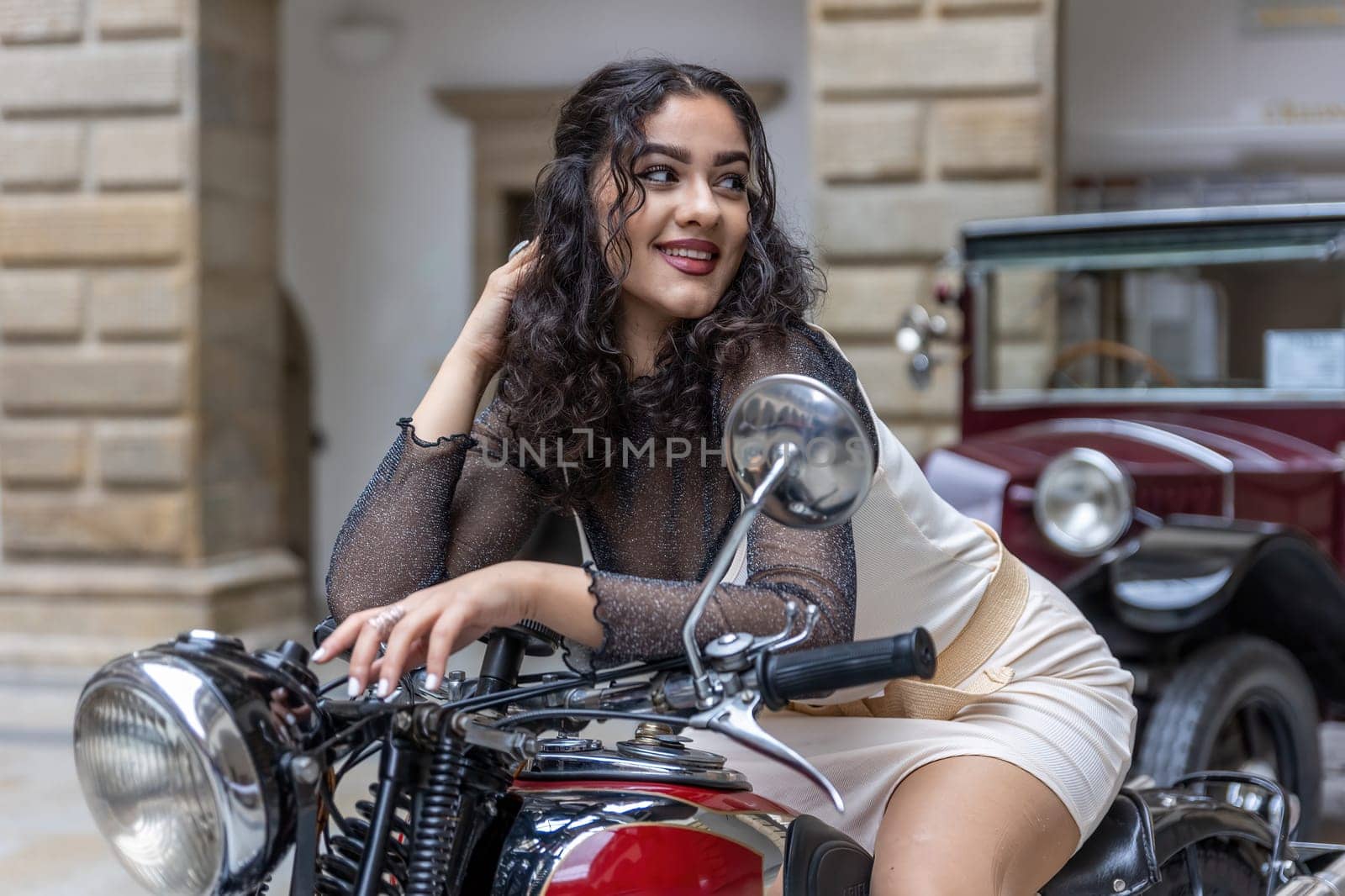 Attractive young woman with long black hair is sitting in a sexy pose on  vintage motorcycle. Horizontally.