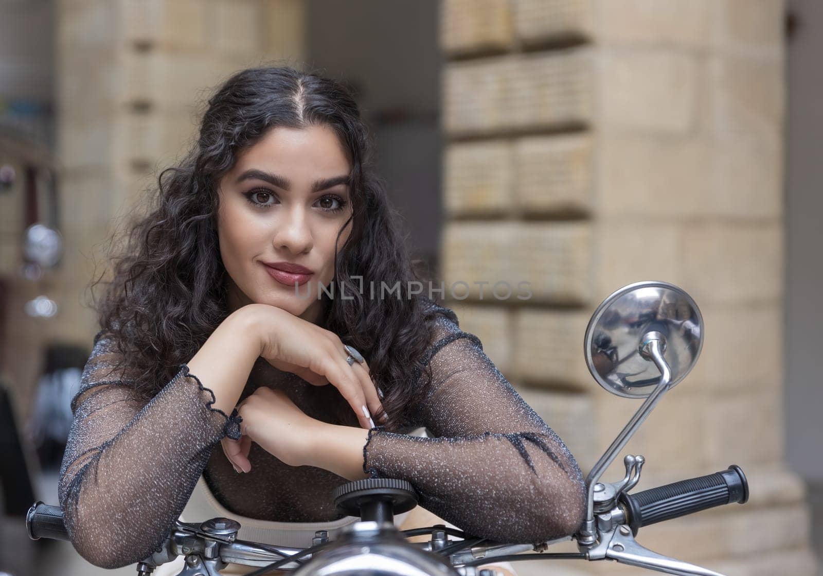Portrait of  tanned girl sitting on a vintage motorcycle looking at the camera. Horizontally.