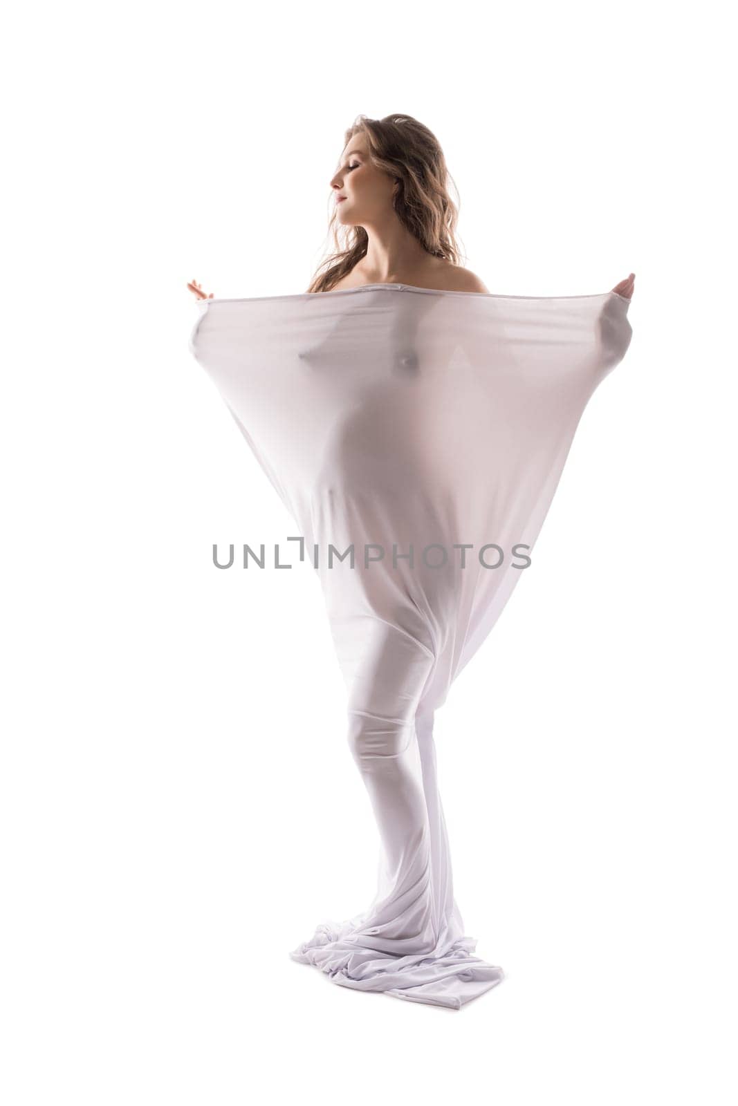 Naked serene pregnant female wrapped in cloth standing with closed eyes on white background in studio
