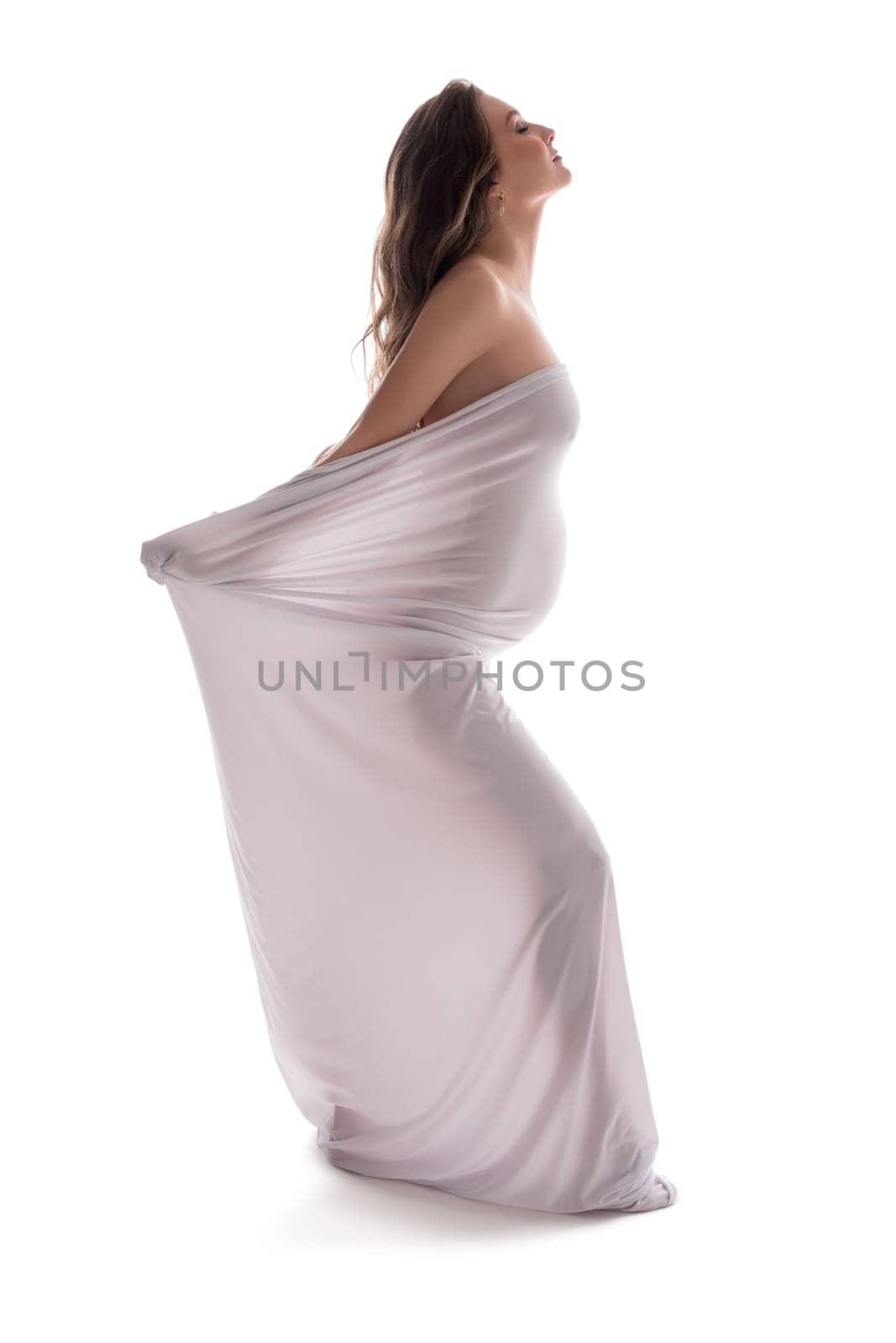 Naked serene pregnant female wrapped in cloth walking with closed eyes on white background in studio