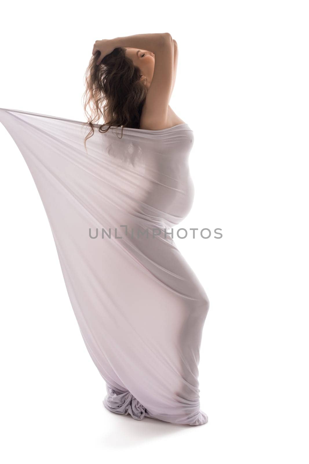 Naked serene pregnant female wrapped in cloth walking with closed eyes on white background in studio