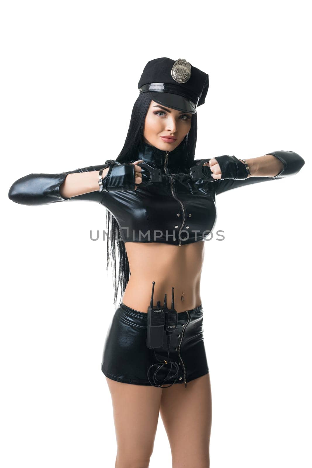 Curvy female wearing black leather police uniform and with handcuffs standing on white background in studio and looking at camera